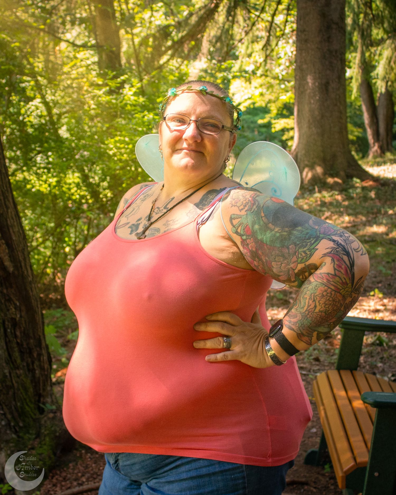 Person in coral top sits contentedly on wooden bench in sunlit forest setting.