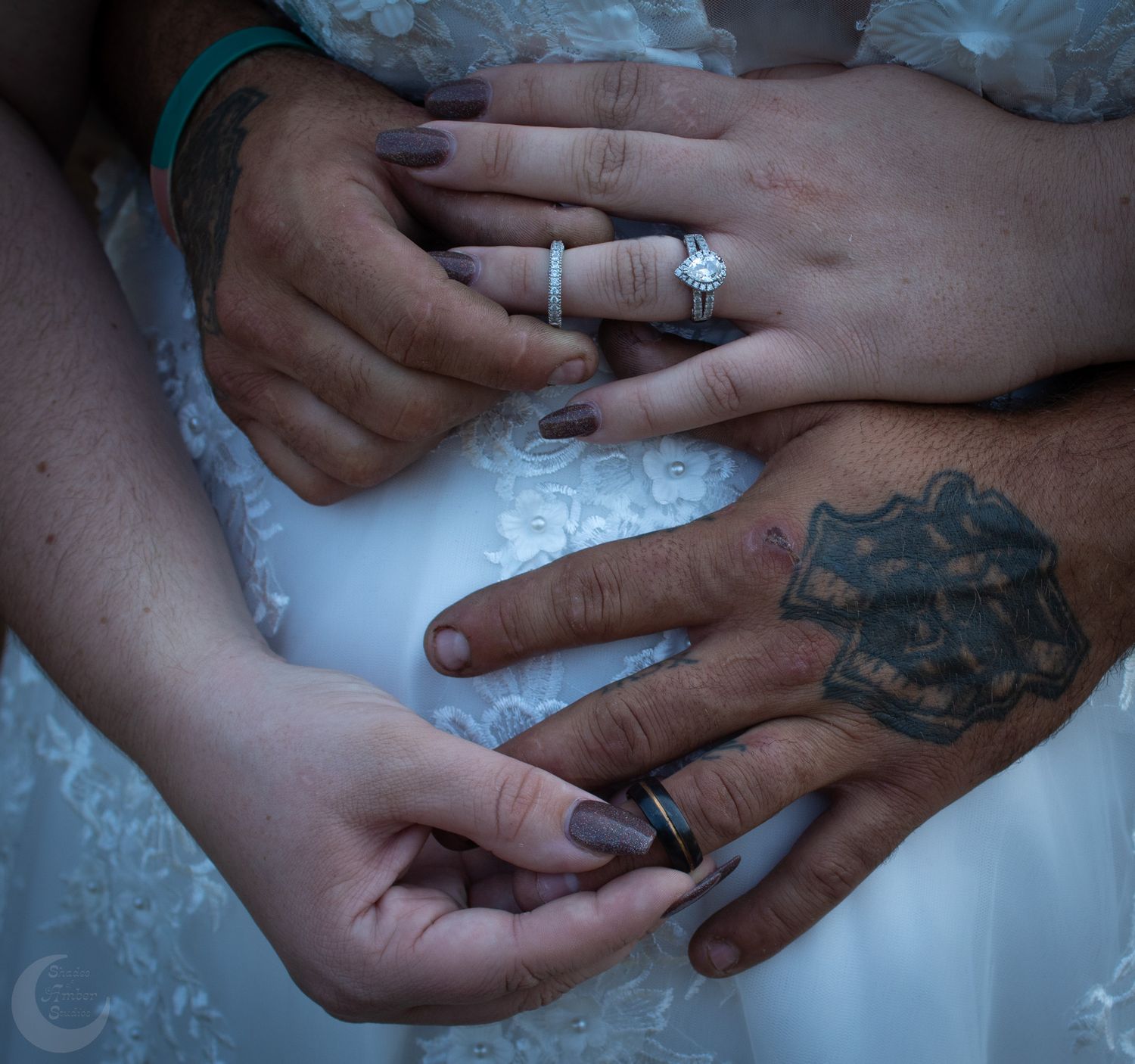 Close-up of hands with tattoos and wedding rings against white fabric.