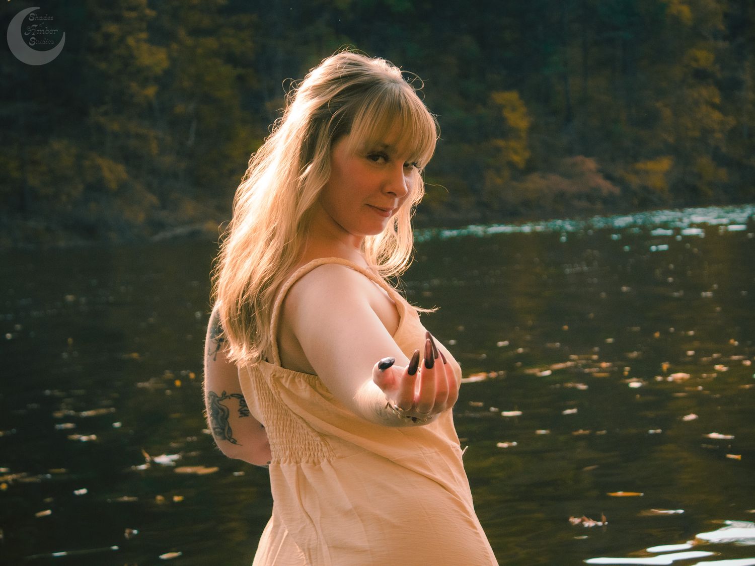 Ethereal portrait in warm light showing a dreamy figure standing by a reflective body of water at dusk.