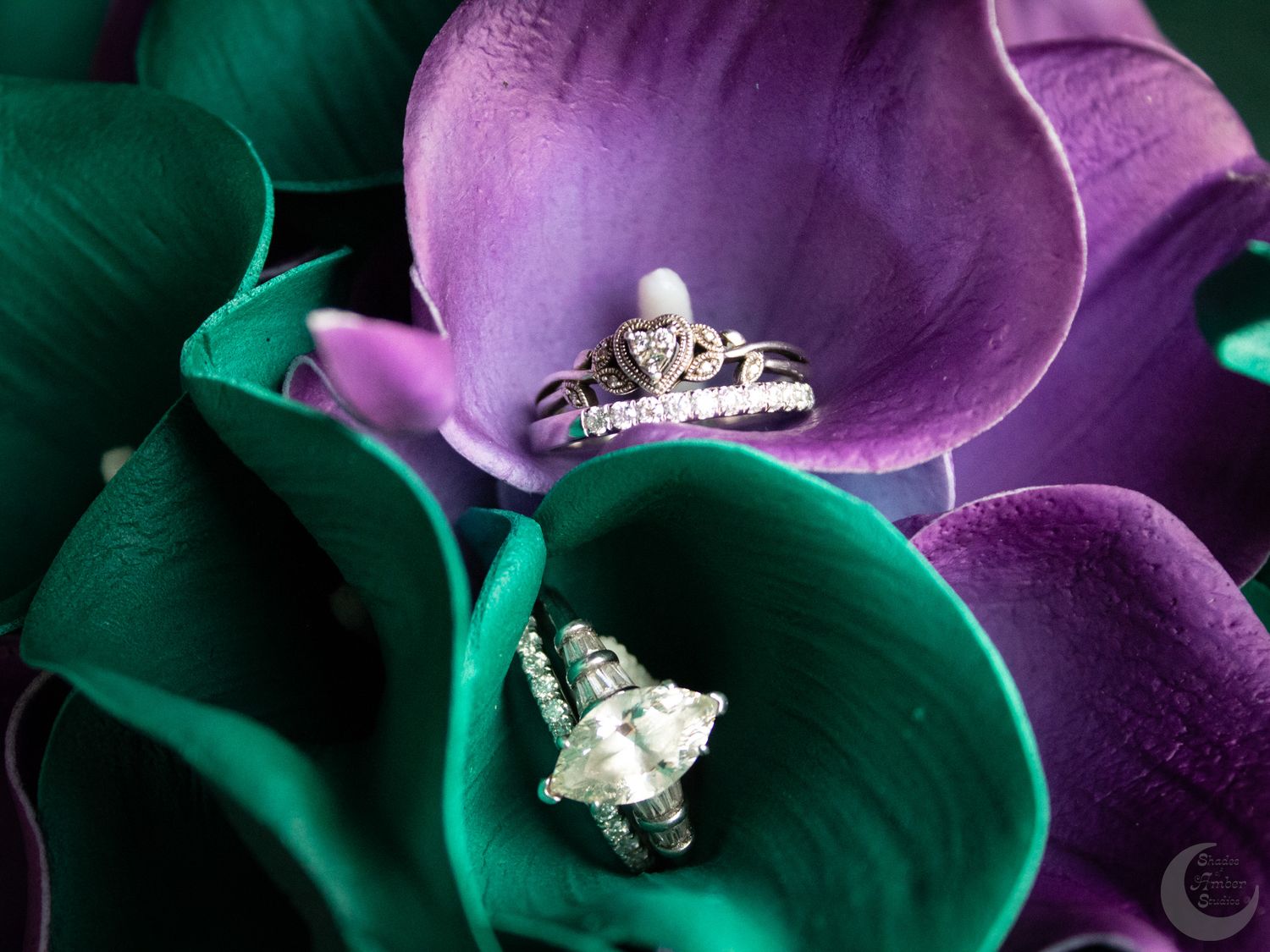 Wedding rings nestled in vibrant purple and green floral petals creating an artistic jewelry display.