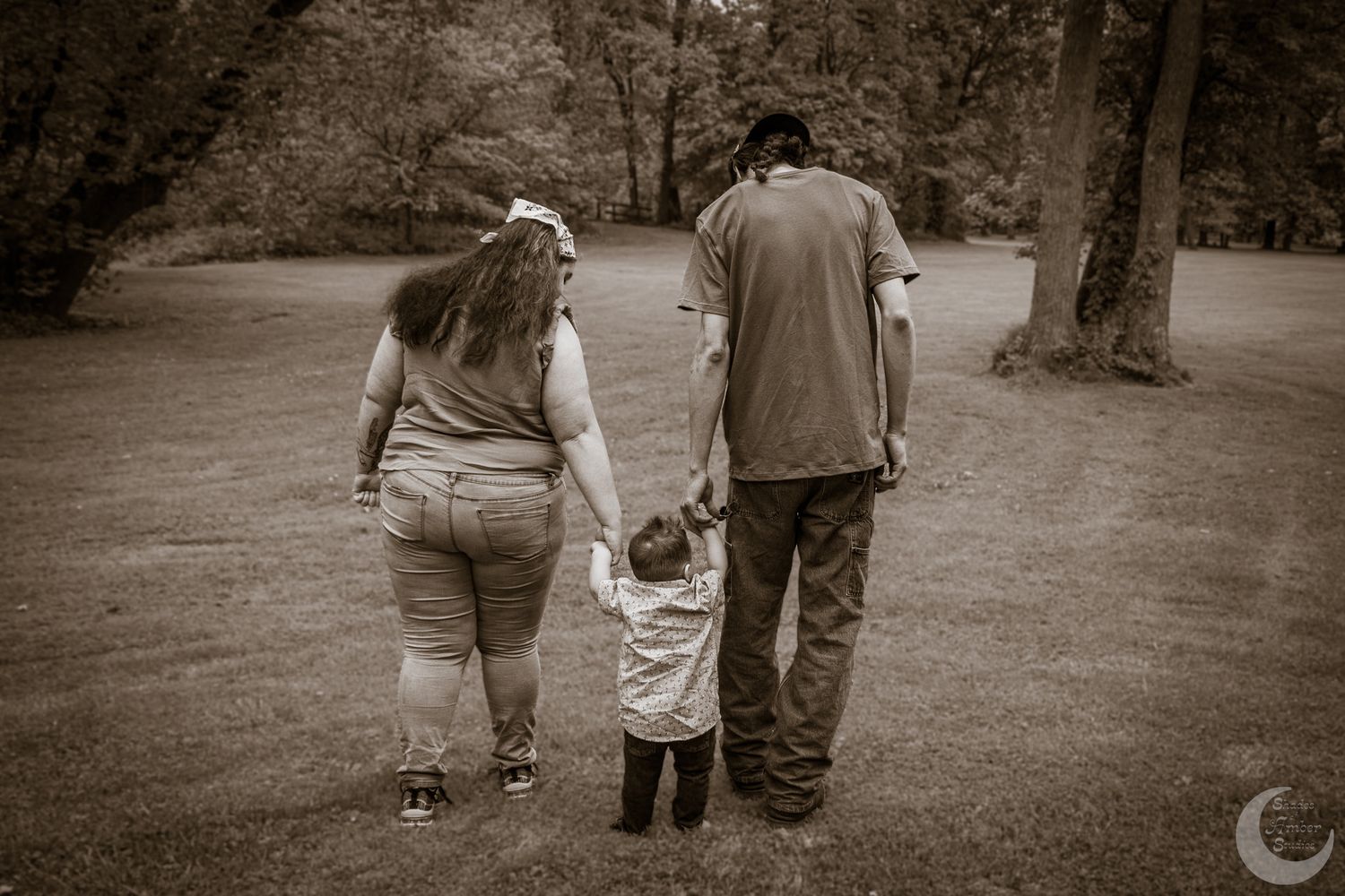 A couple walks hand in hand along a tree-lined path in a black and white photograph.