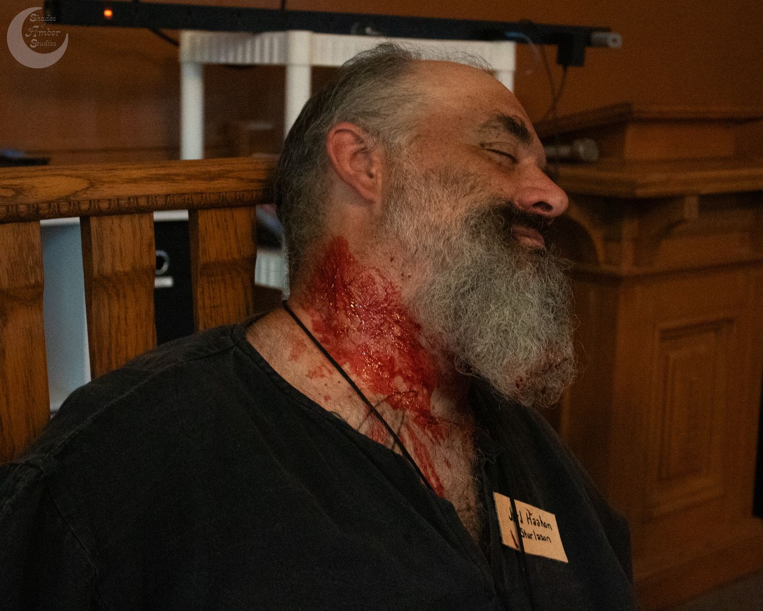 A bearded man with a blood-covered face in a dimly lit rustic wooden environment.