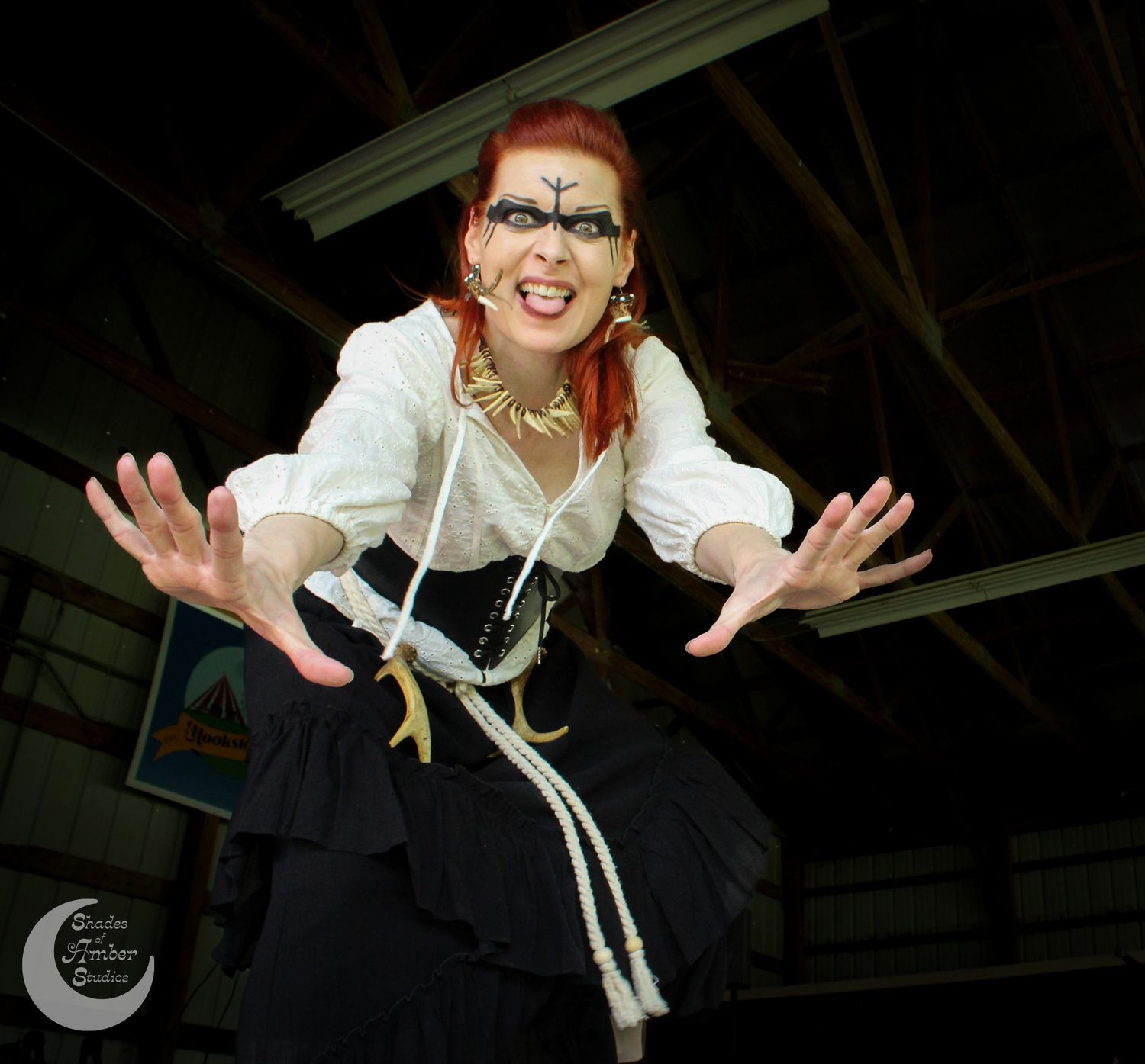 Someone in theatrical steampunk costume with white blouse, black skirt and dramatic makeup poses dramatically in dimly lit space.