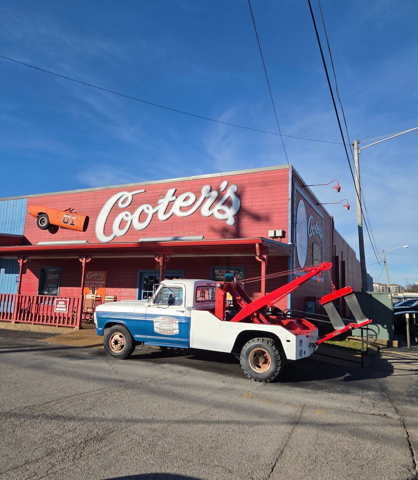 A vintage blue and white pickup truck parked in front of Cooter's restaurant with its hood open under a bright blue sky.