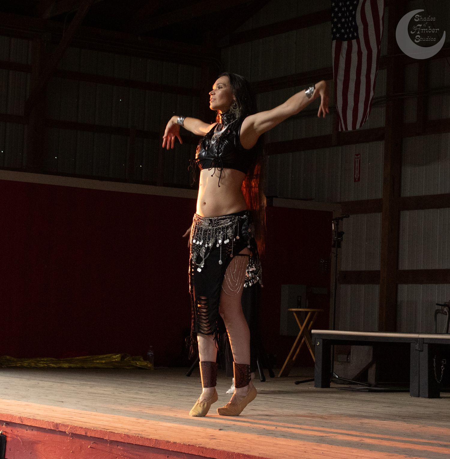 A belly dancer performs gracefully on stage with dramatic lighting and an American flag in the background.