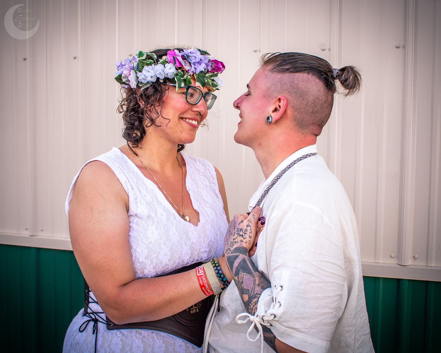 Two people in white outfits share a joyful moment together, one wearing a floral crown in their curly hair.