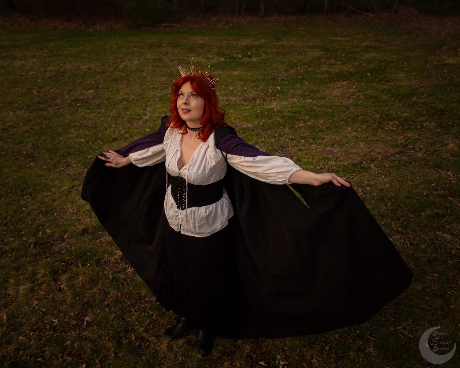 Figure in cosplay attire with flowy black skirt and white corset poses gracefully in a grassy outdoor setting.