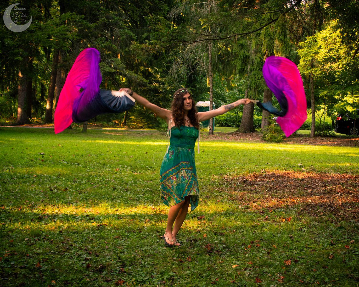 A dancer performs with flowing pink fabric in a sunlit forest clearing.