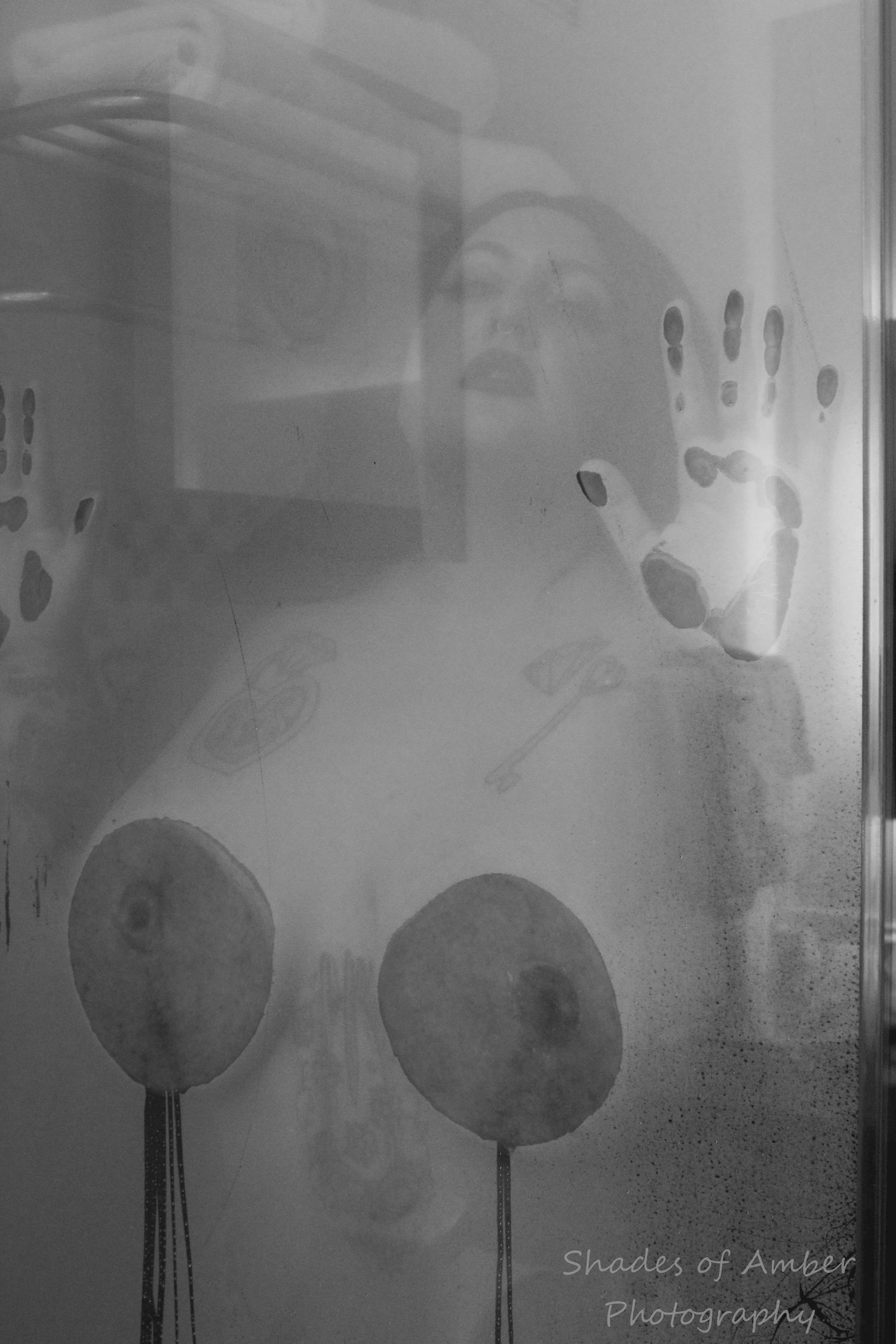 Artistic black and white photography of a steamy shower glass with handprints and circles visible through the condensation.