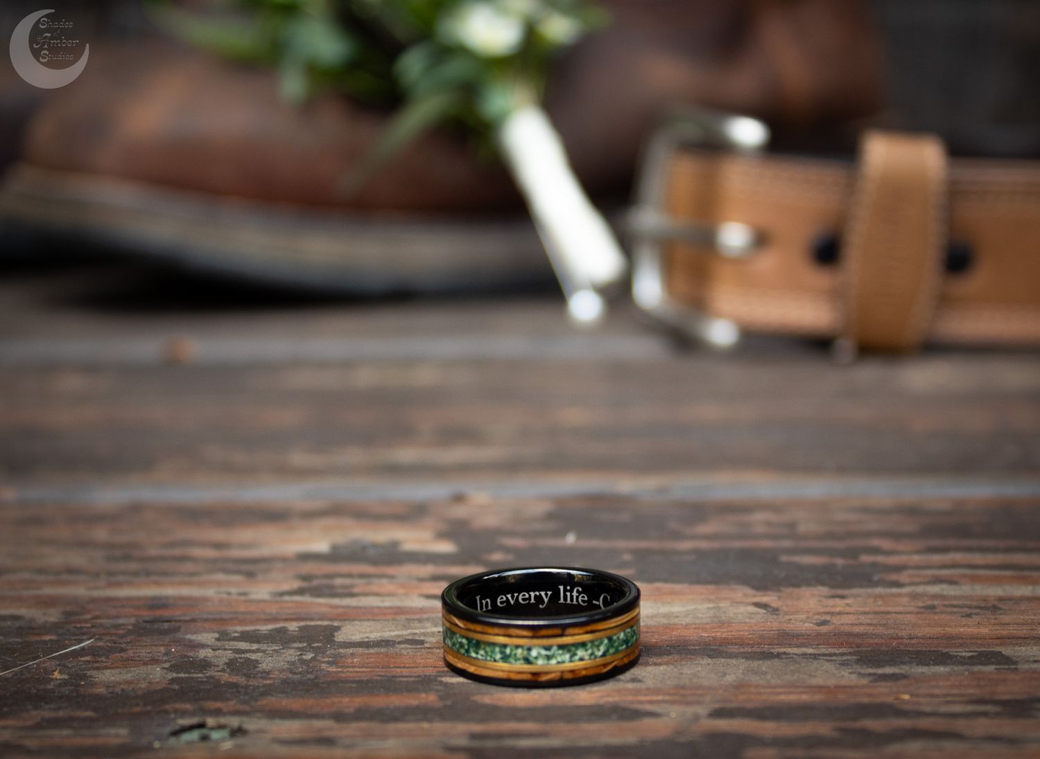 Golden wedding band with dark green inlay rests on rustic wooden surface in soft lighting.