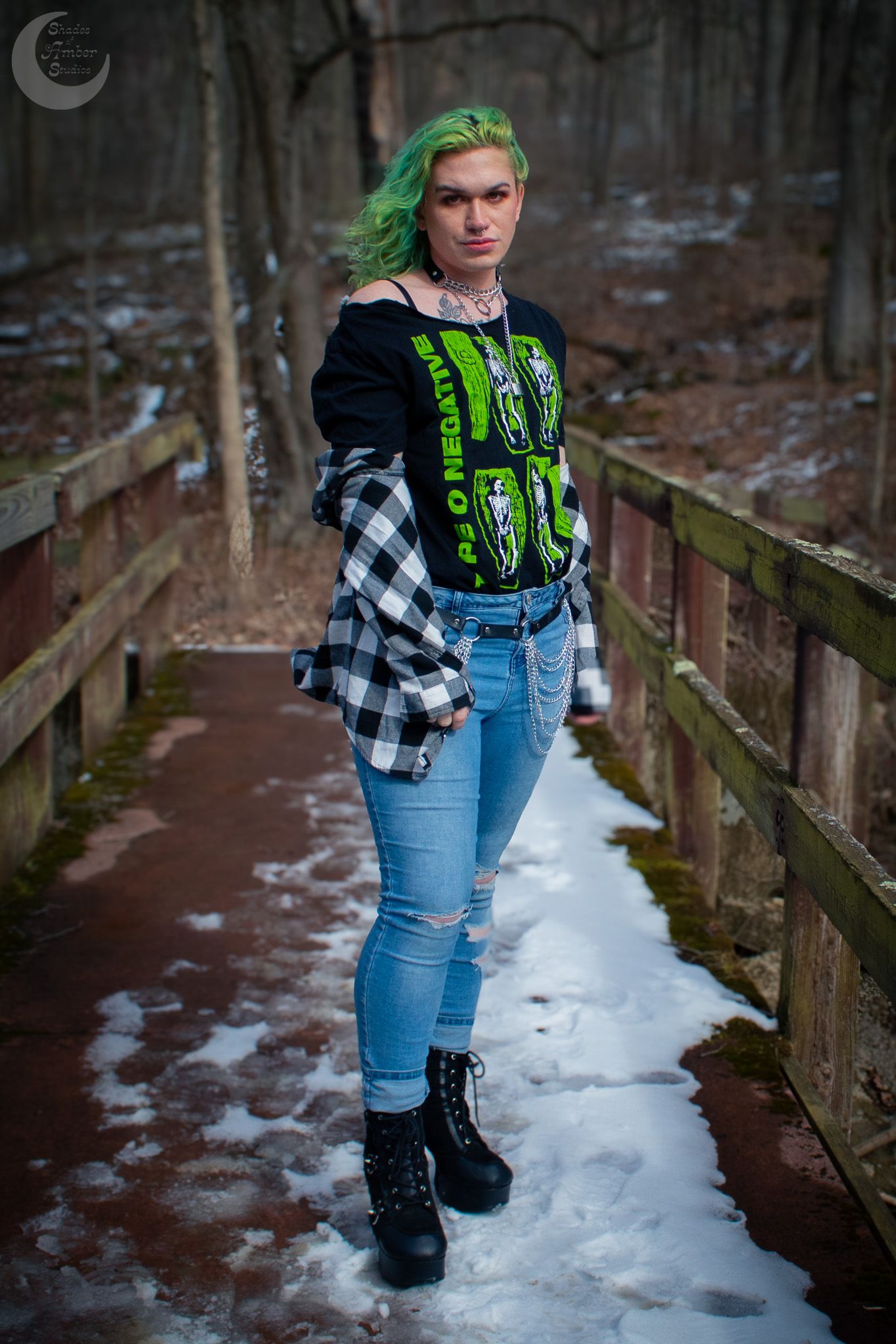 Winter fashion shot on snowy wooden bridge with plaid shirt and graphic tee.