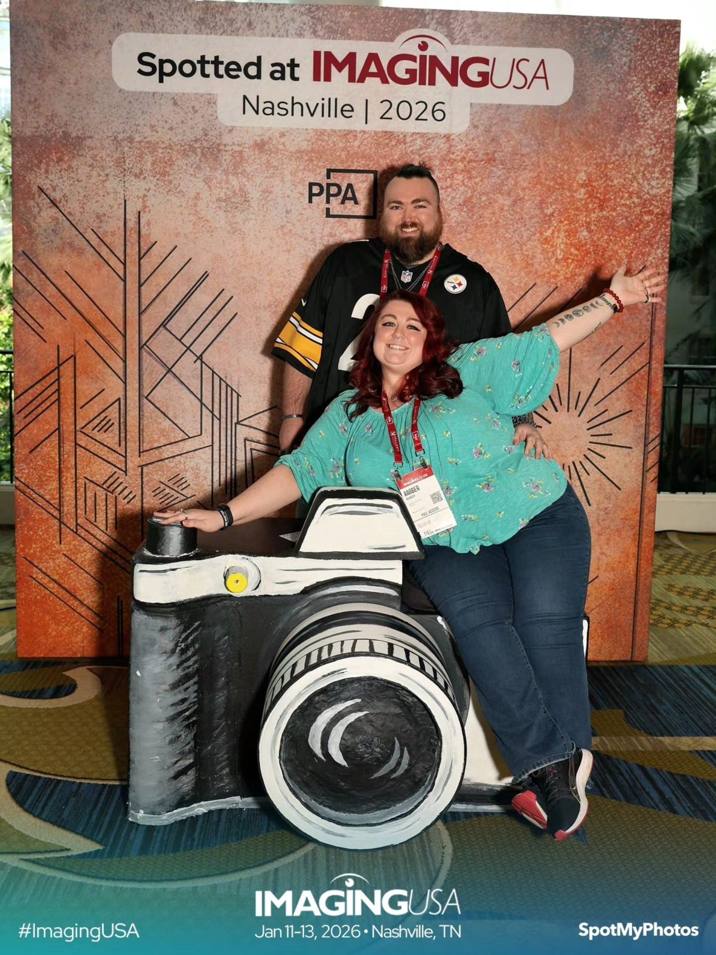 People pose playfully with a large decorative camera prop at a photo booth with geometric wall art in the background.