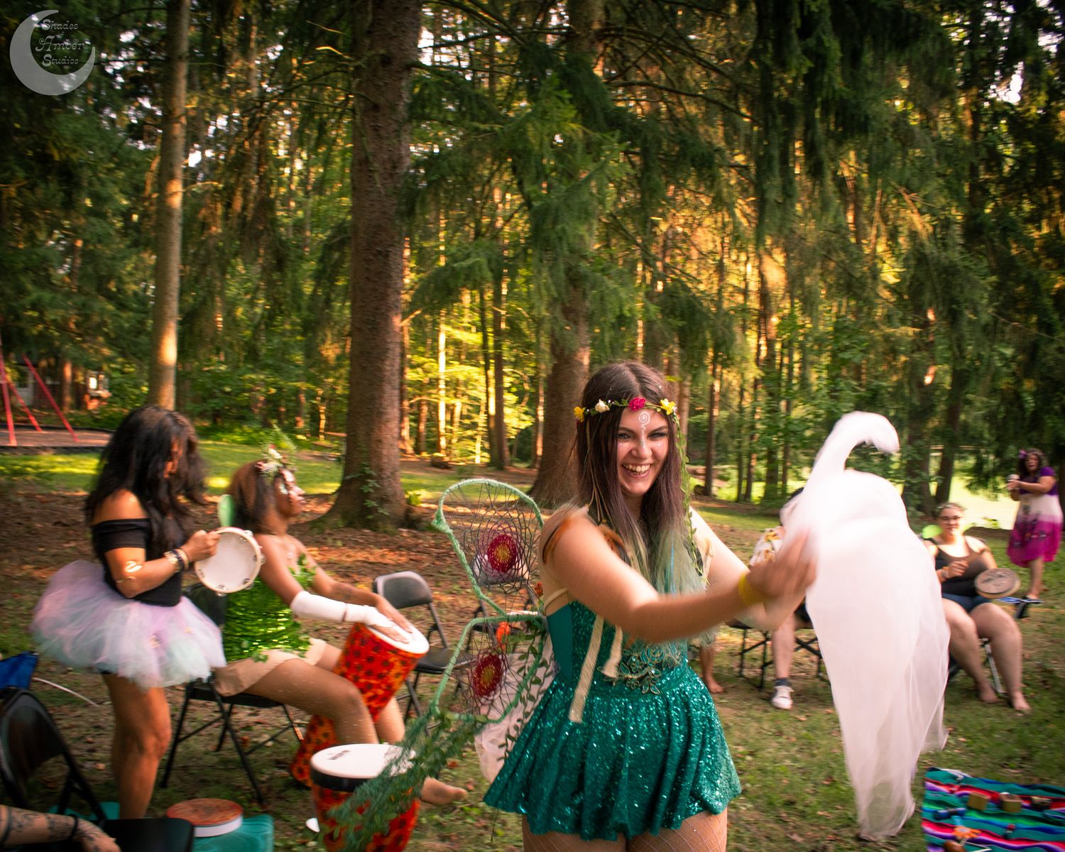 People enjoying a playful summer gathering in a sunlit forest with whimsical decorations and outdoor seating.