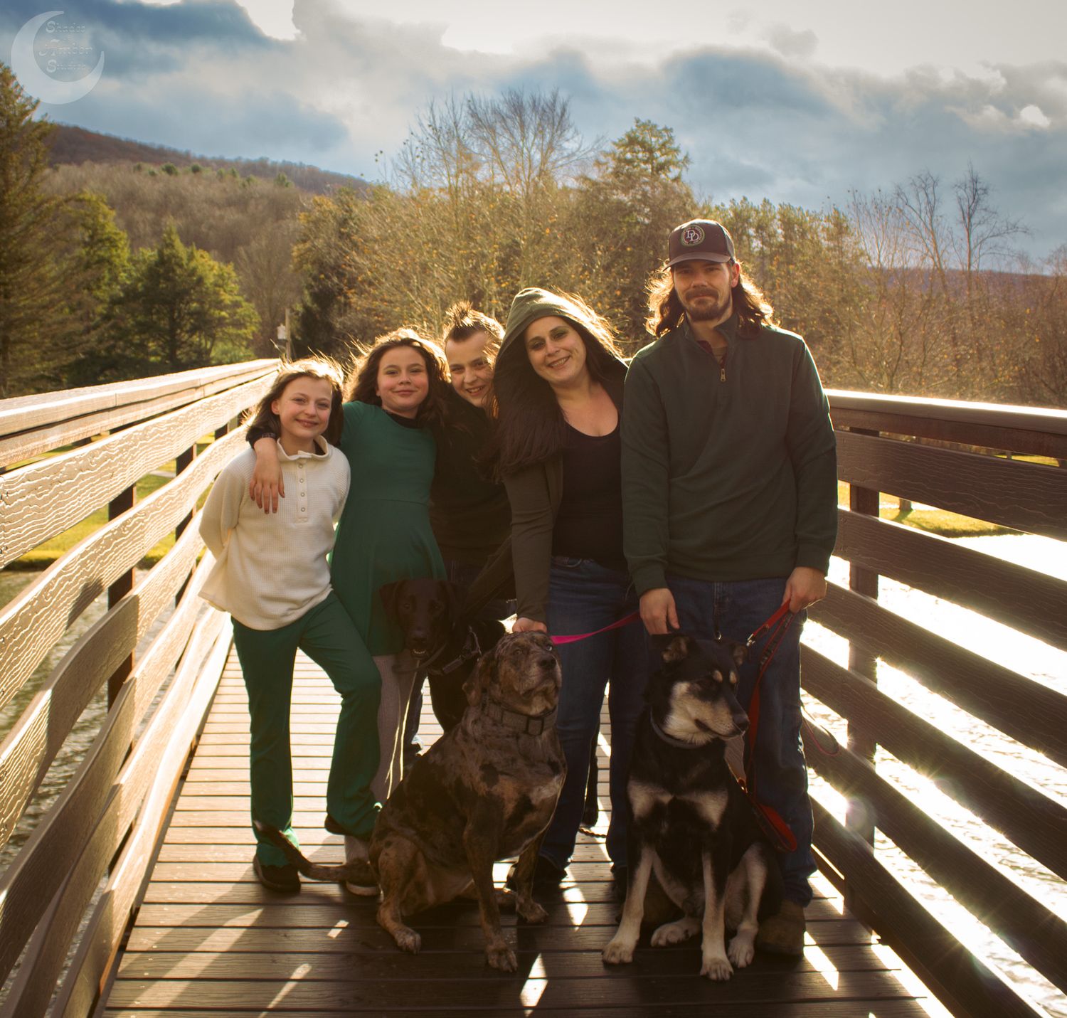 A group stands with two dogs on a wooden bridge overlook in the mountains on a sunny autumn day.