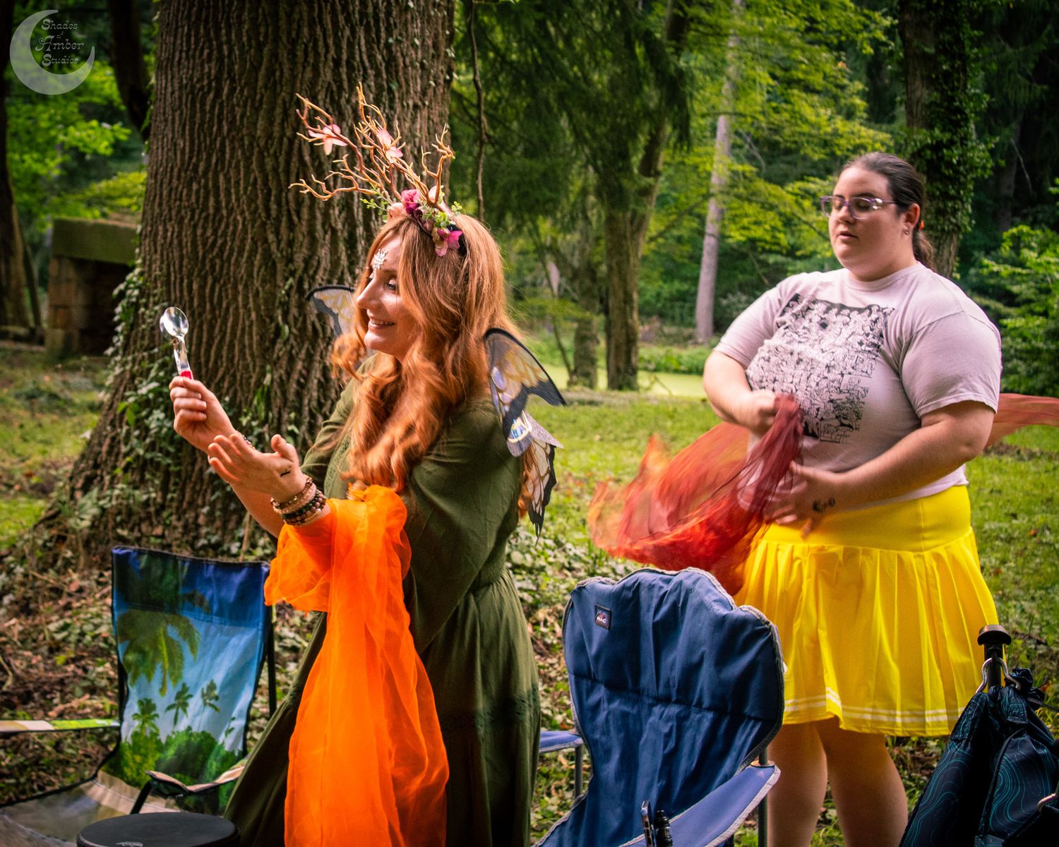 Friends in bright orange and blue dresses pose playfully in a sunny park setting.