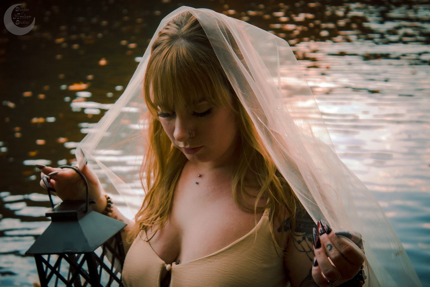 Atmospheric portrait with vintage lantern and veil beside dark water at dusk.