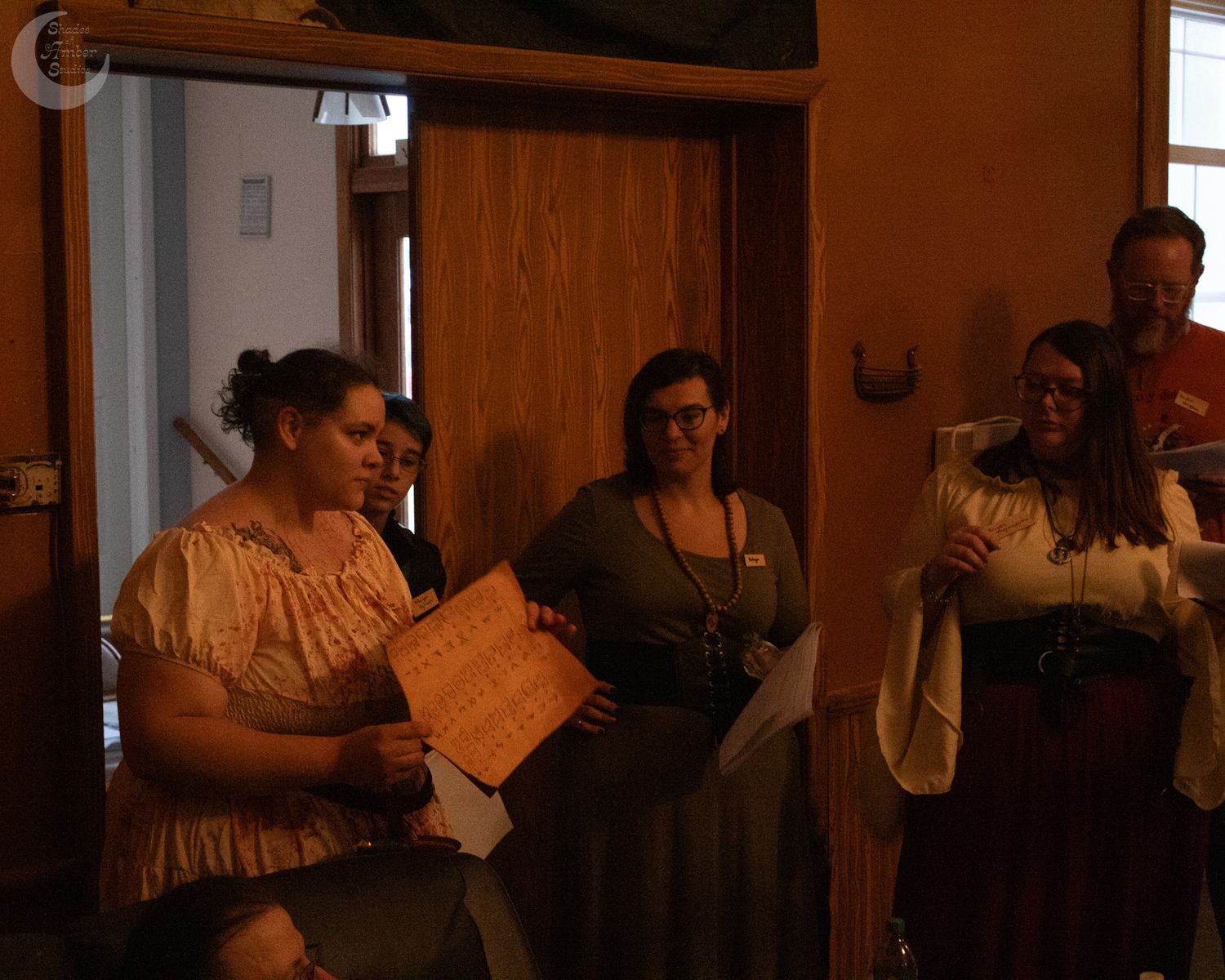 People gather in a dimly lit hallway with wood beam ceilings and warm orange walls.