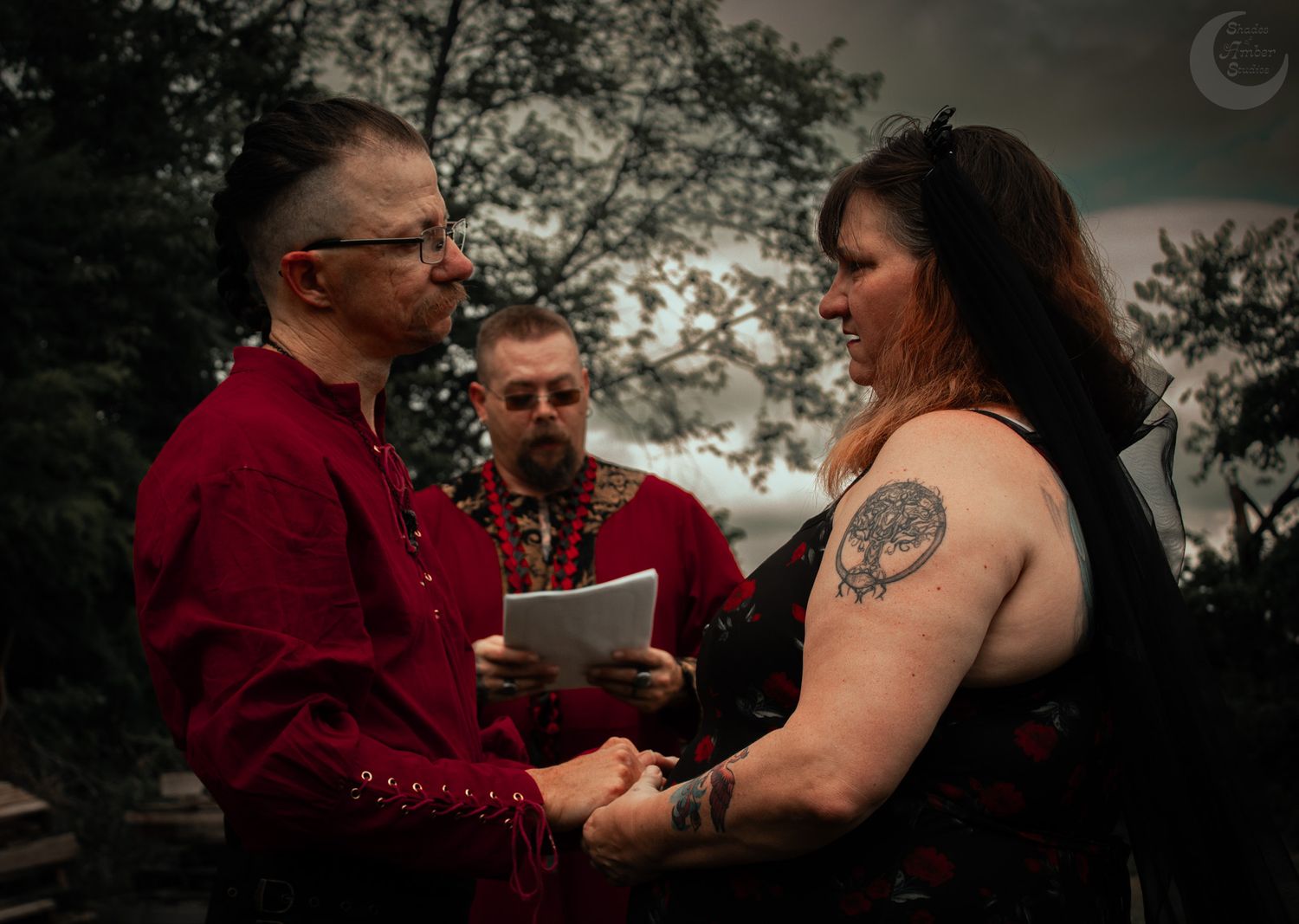 A couple in dark red attire holding hands during their outdoor wedding ceremony at dusk.