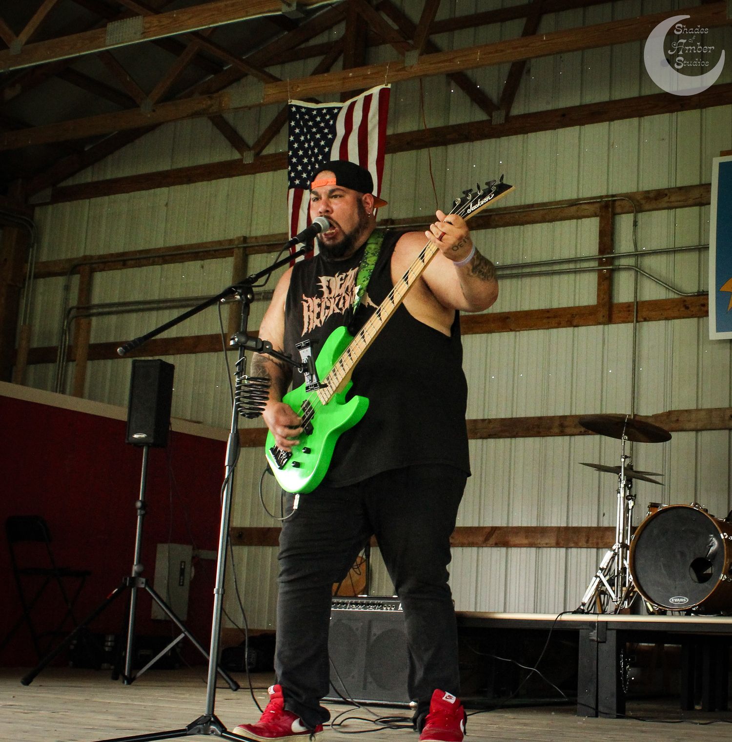 Musician performs on stage with bright green electric guitar in front of American flag at indoor venue.
