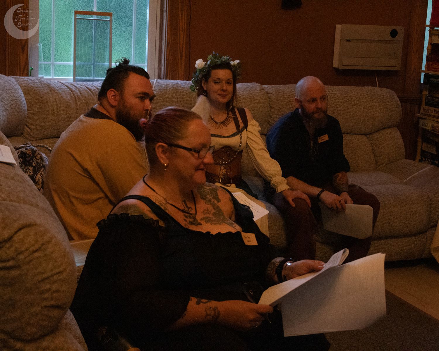 A group of people sitting on a beige couch in a dimly lit living room while looking at a laptop.