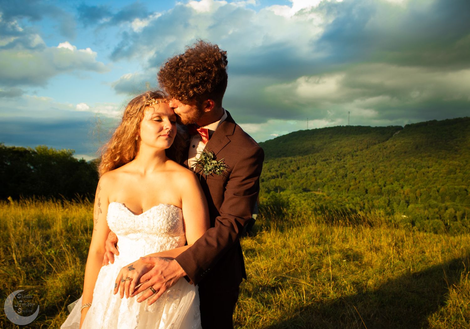 Sunset wedding portrait on a hilltop with dramatic clouds and mountain backdrop.