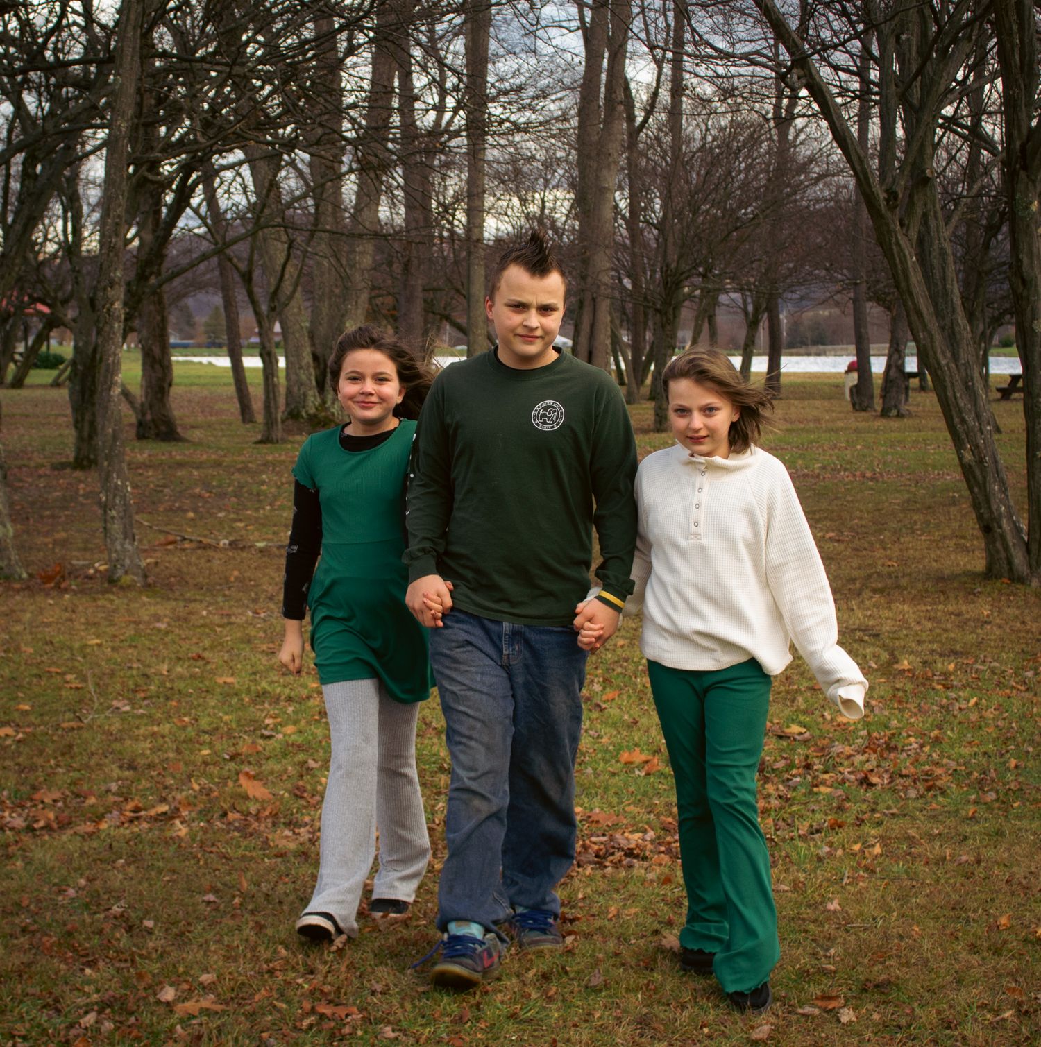 A group of people walking together through a park with bare trees and fallen leaves on an autumn day.