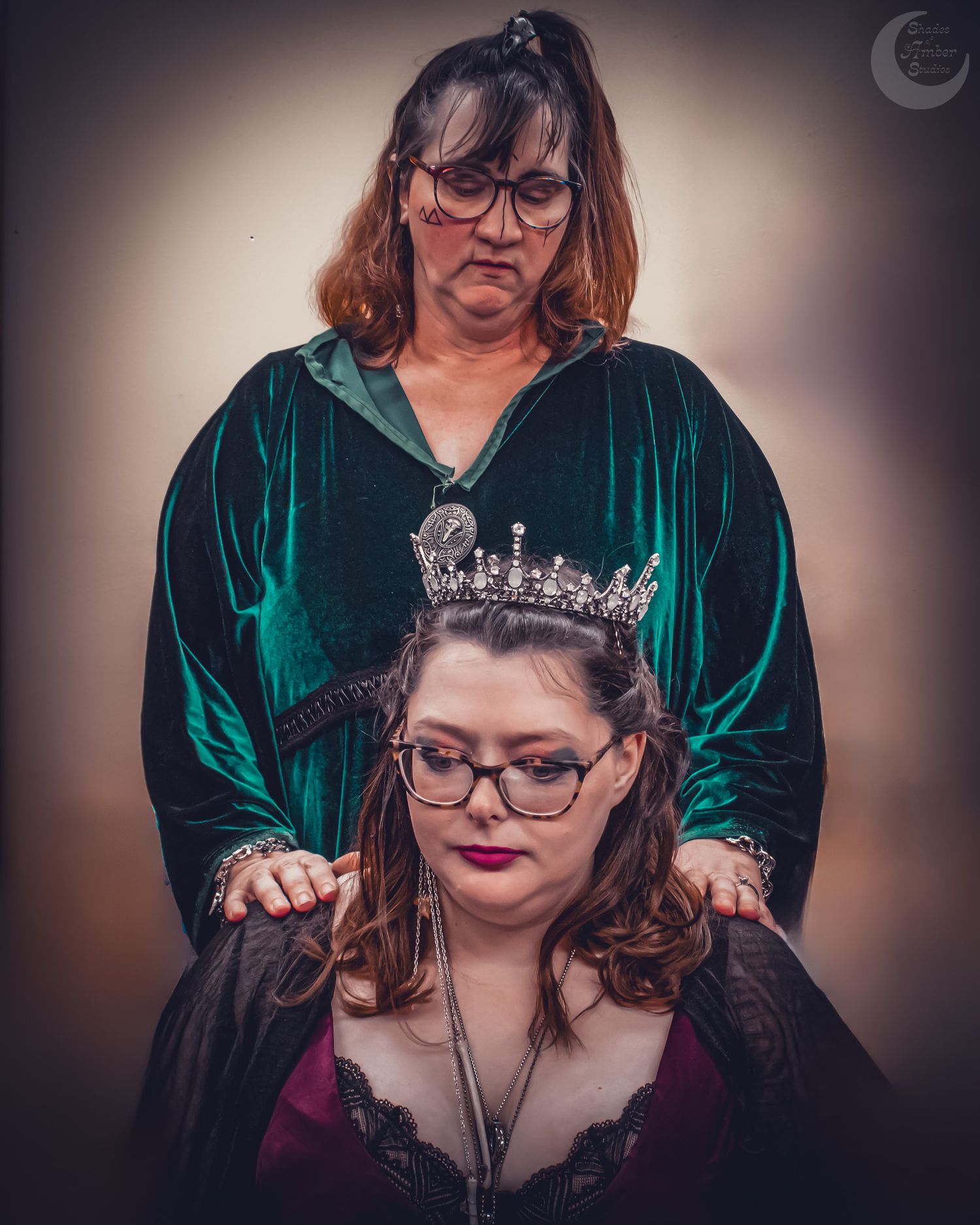 A regal portrait showing someone wearing a jeweled crown and emerald green velvet gown with another person standing behind.
