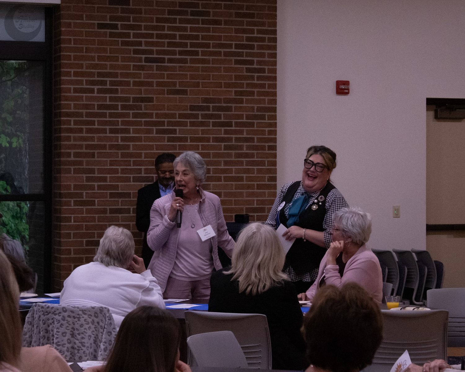 People engaged in discussion during a meeting in a room with brick walls and round tables.
