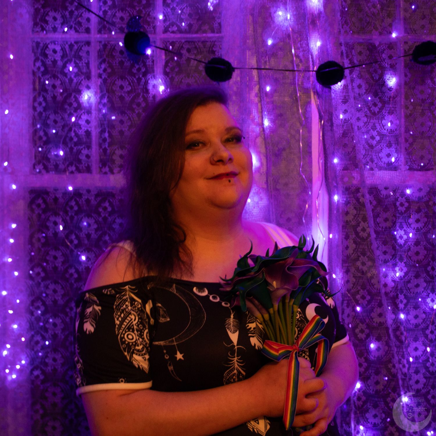 A portrait against a purple sparkly backdrop with black floral accents and dramatic lighting.