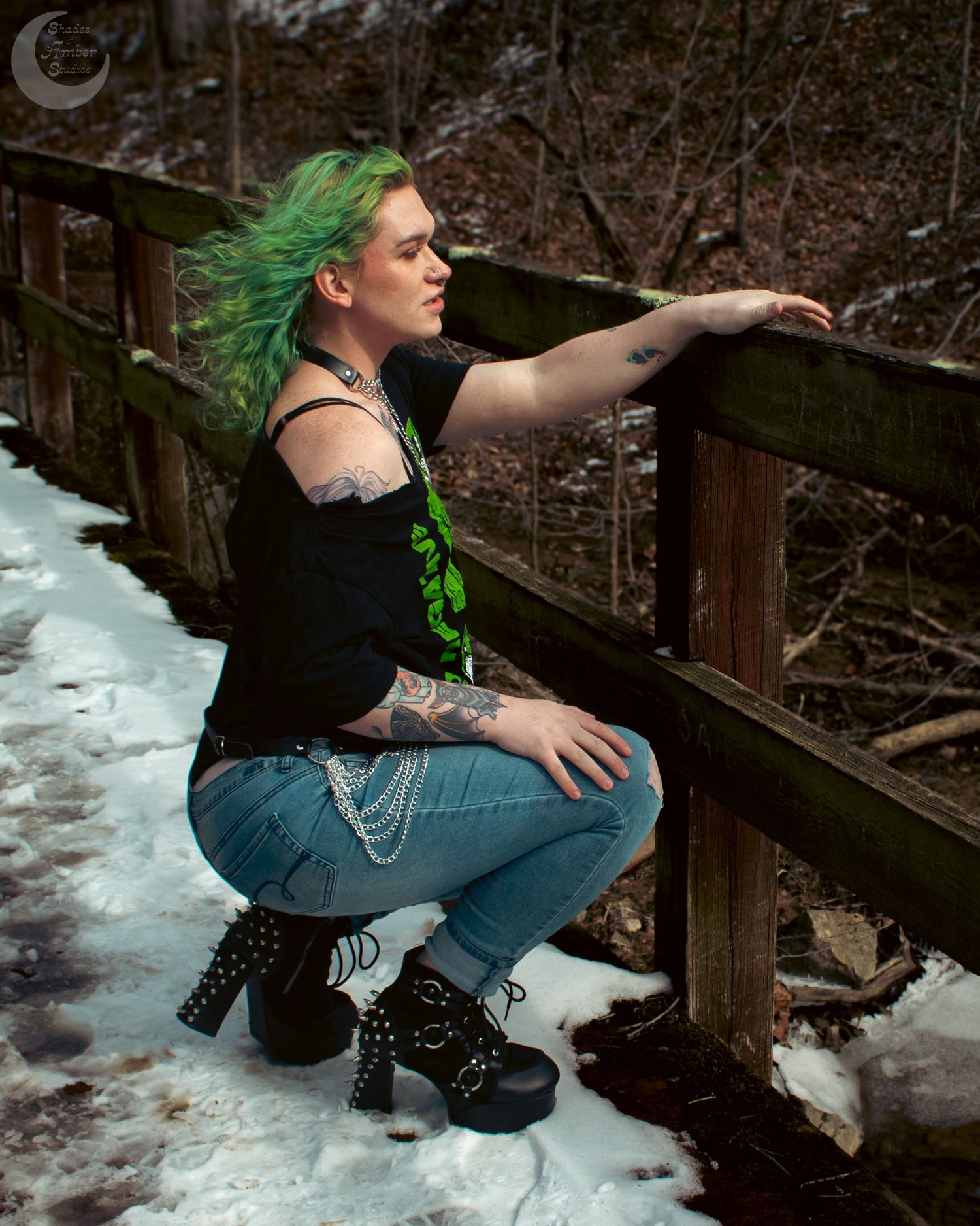 Expressive pose on snowy wooden bridge railing in alternative fashion style.
