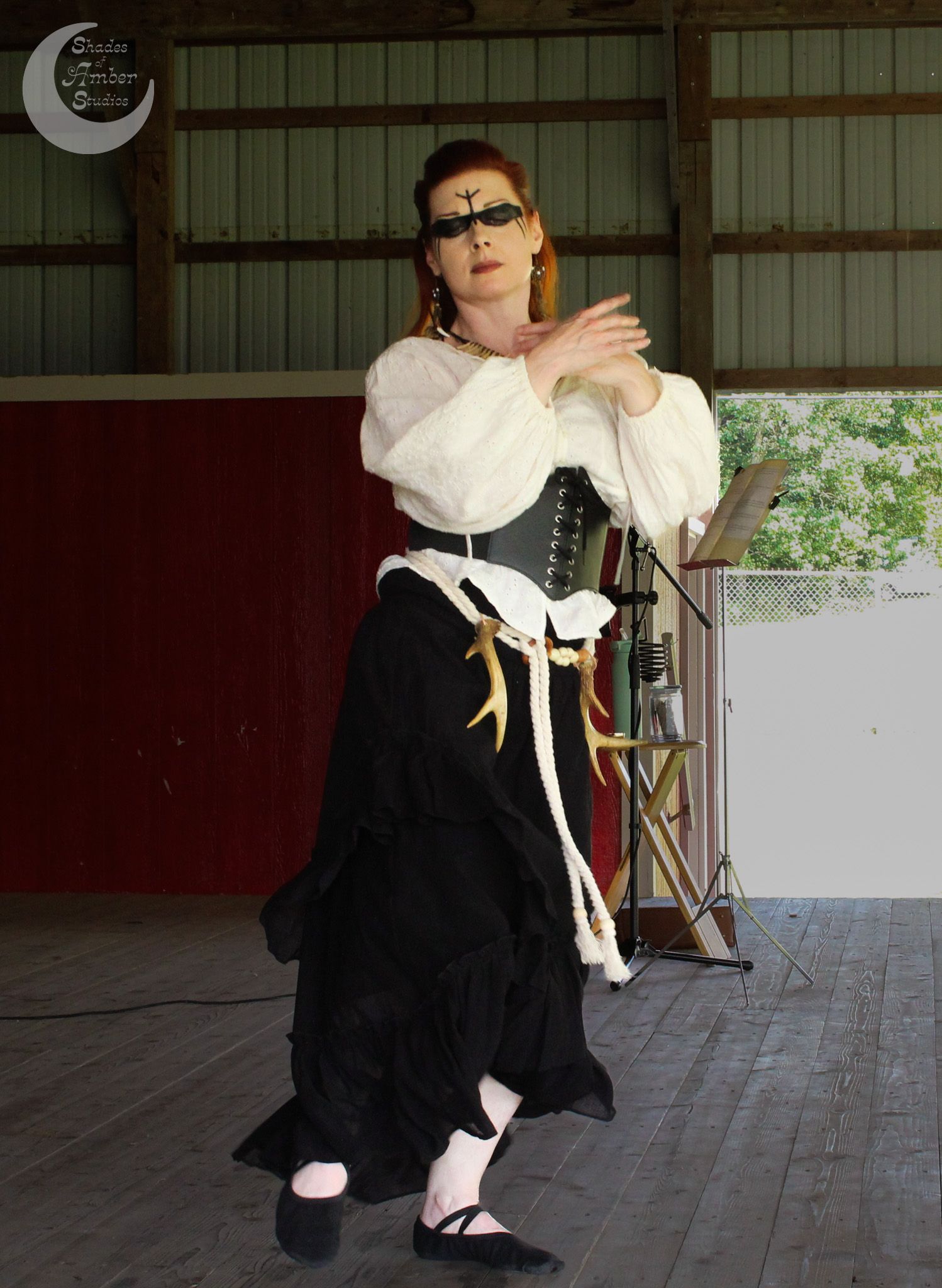 A dancer in Victorian-inspired costume with white blouse, black skirt and corset performs on a wooden stage.