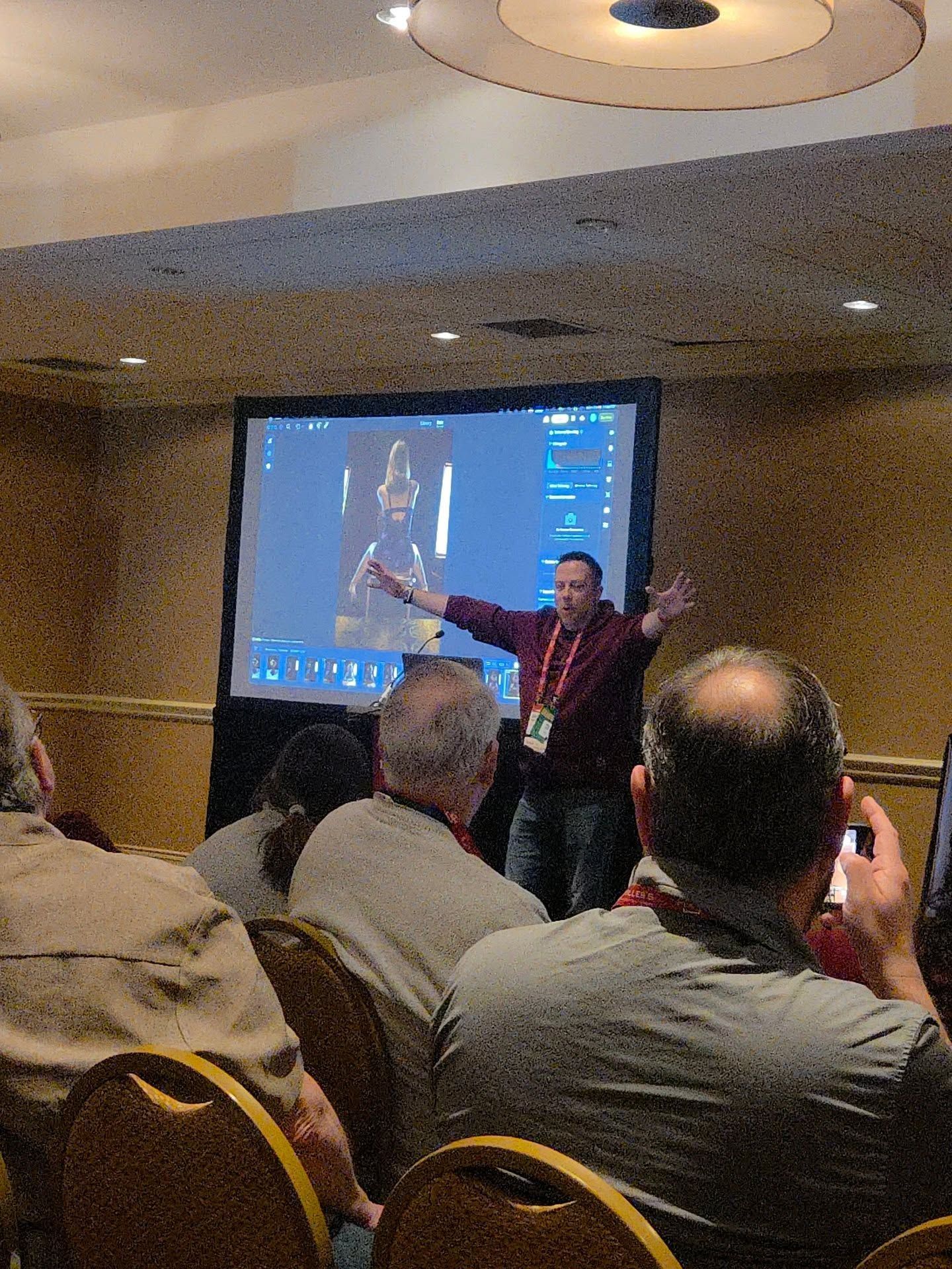 A group of people seated in a conference room watching a presentation on a large screen at the front.
