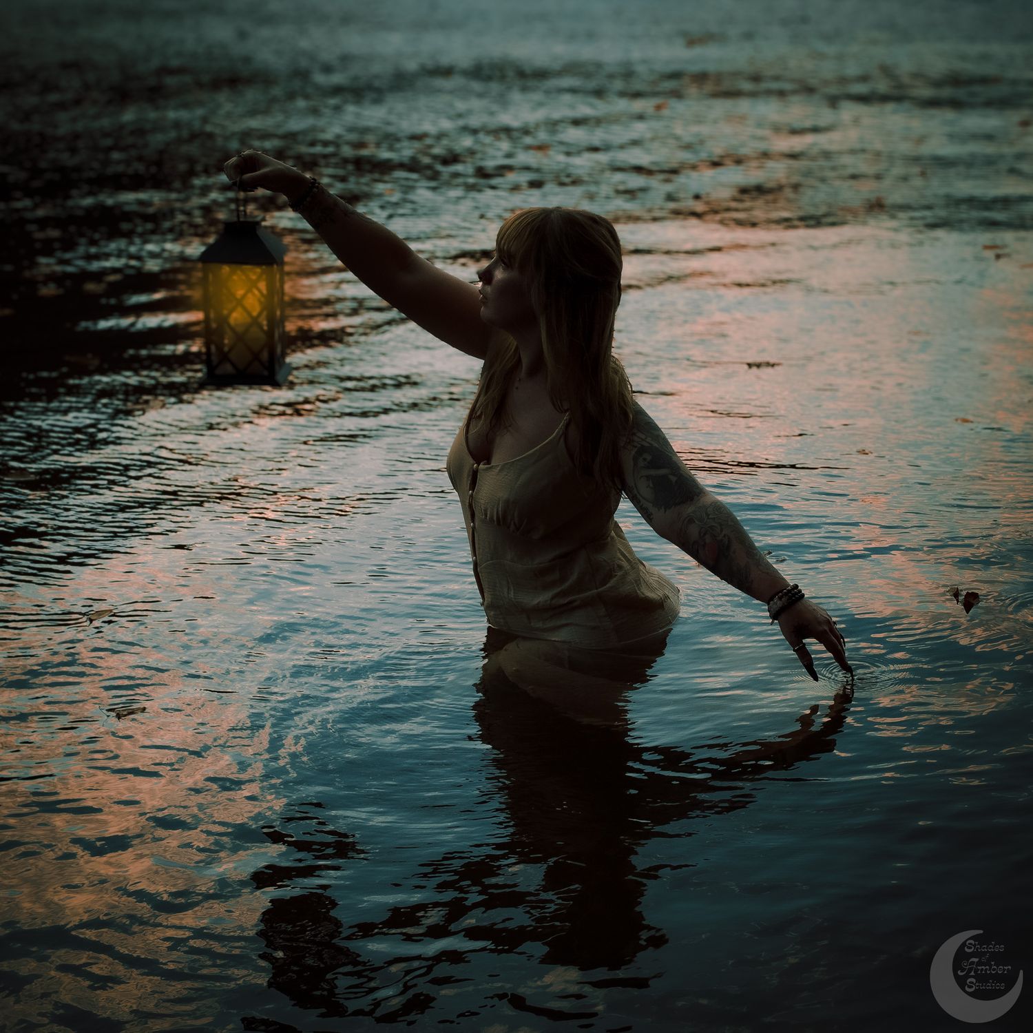 A silhouetted figure wades through reflective water at sunset while holding a glowing lantern overhead.