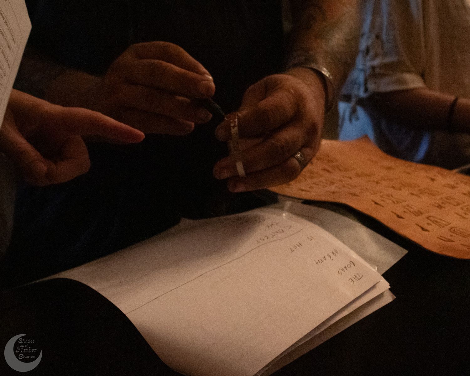 Close-up of hands holding pen and paper in low light, reviewing or signing documents at a desk.