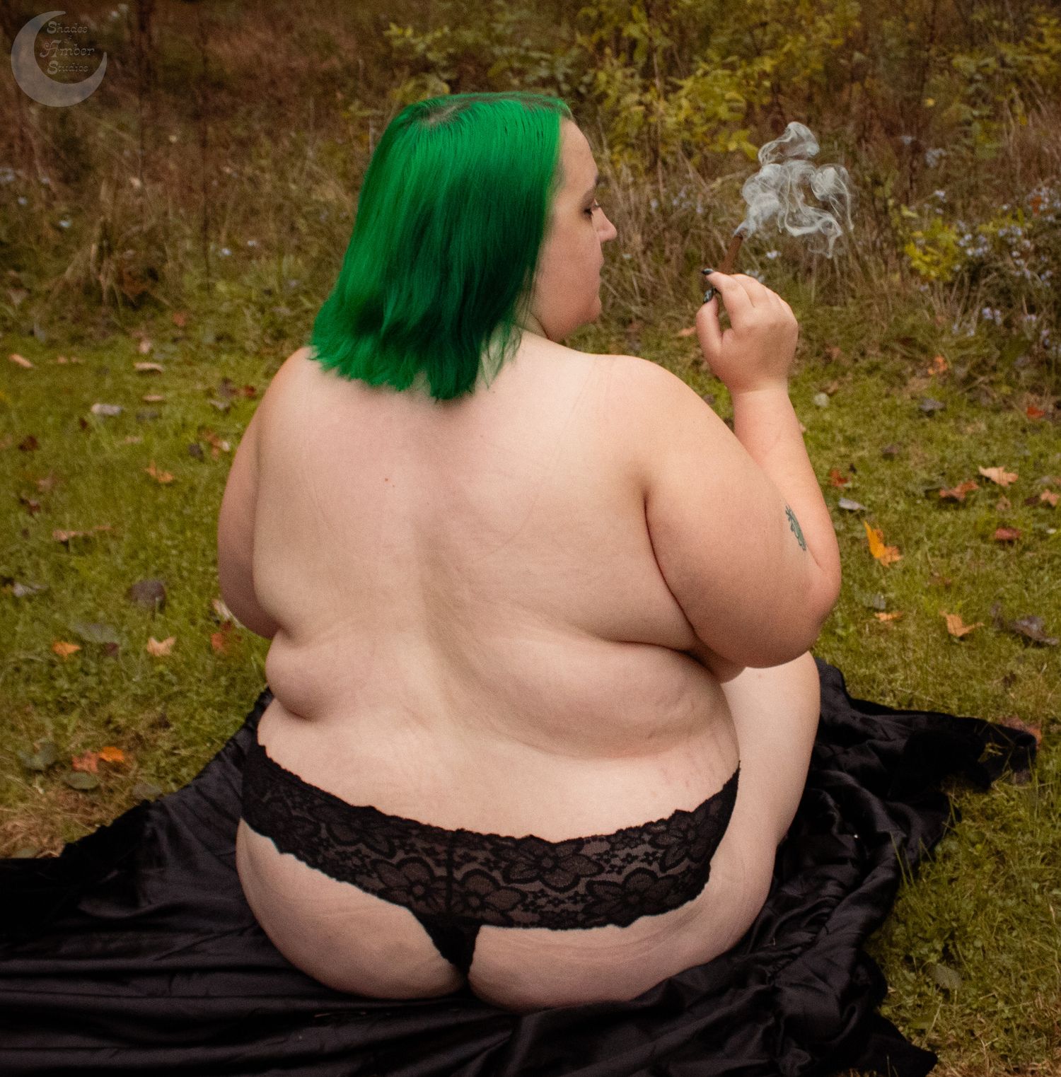 Figure with green hair reclining on black fabric outdoors.