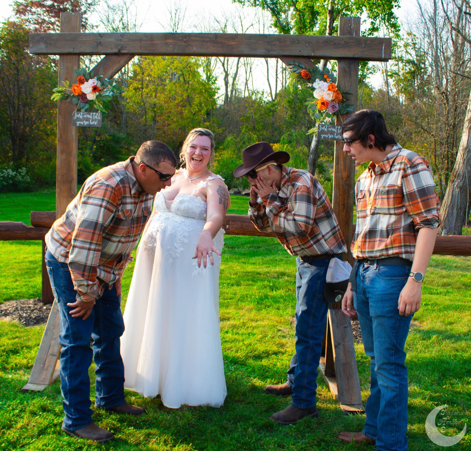 Fun wedding photo with group in matching plaid shirts under wooden arch.