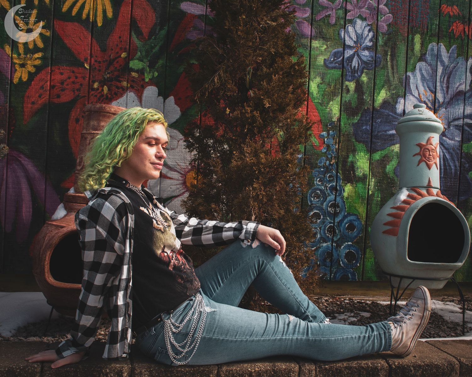 Casual portrait with plaid shirt and jeans lounging by artistic outdoor decoration.