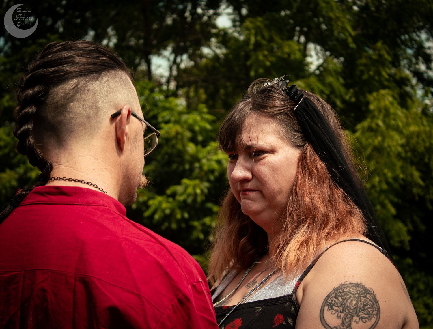 A couple shares an intimate outdoor moment in a green park setting wearing matching vibrant red clothing.