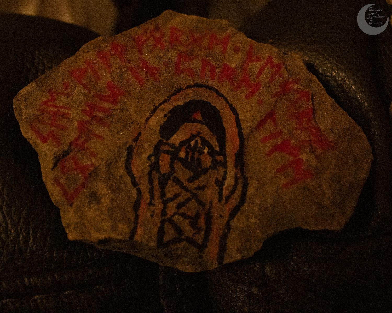 A weathered stone fragment displays ancient runic markings and symbols in red and black colors.