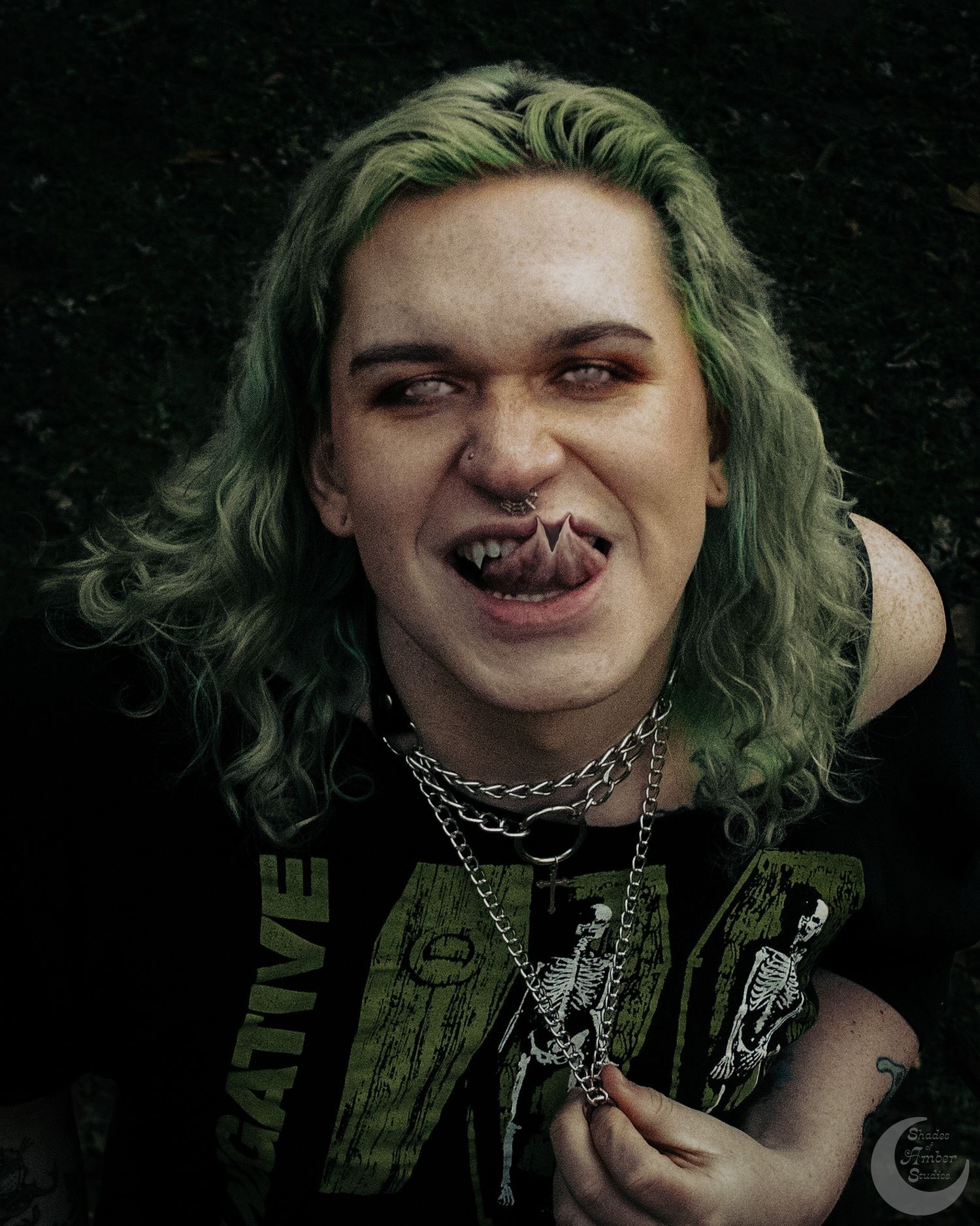 Alternative style portrait with bright green hair, chains and dark clothing against black background.