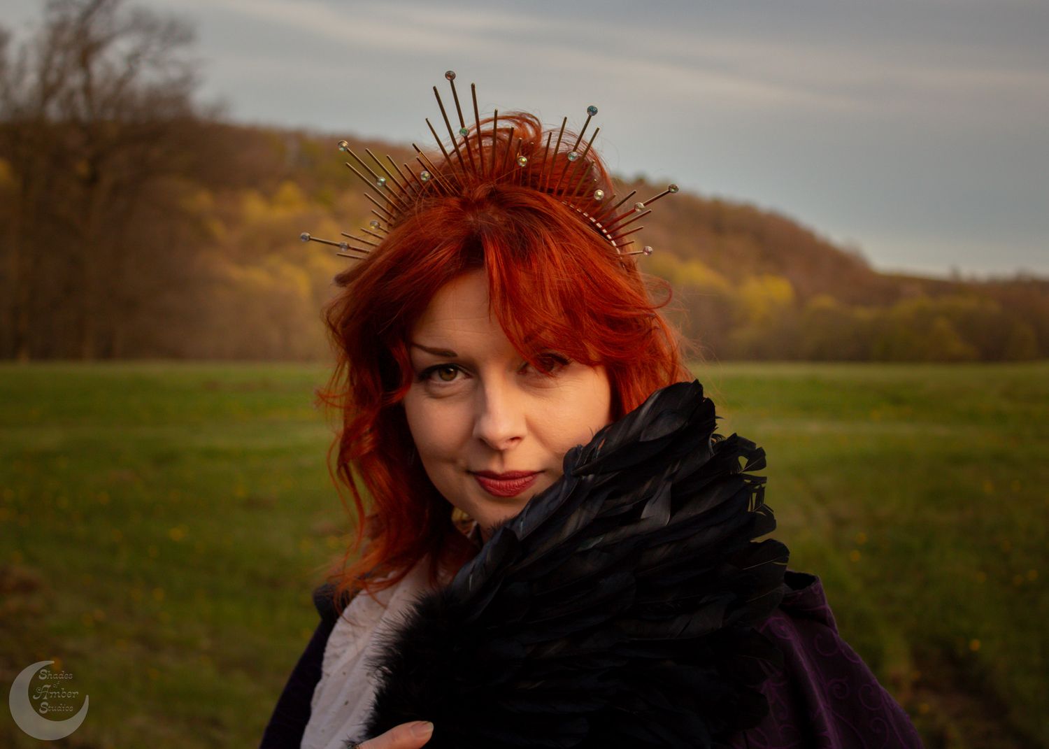 A gothic-inspired portrait with red hair and black feathered accessories in a rural setting.