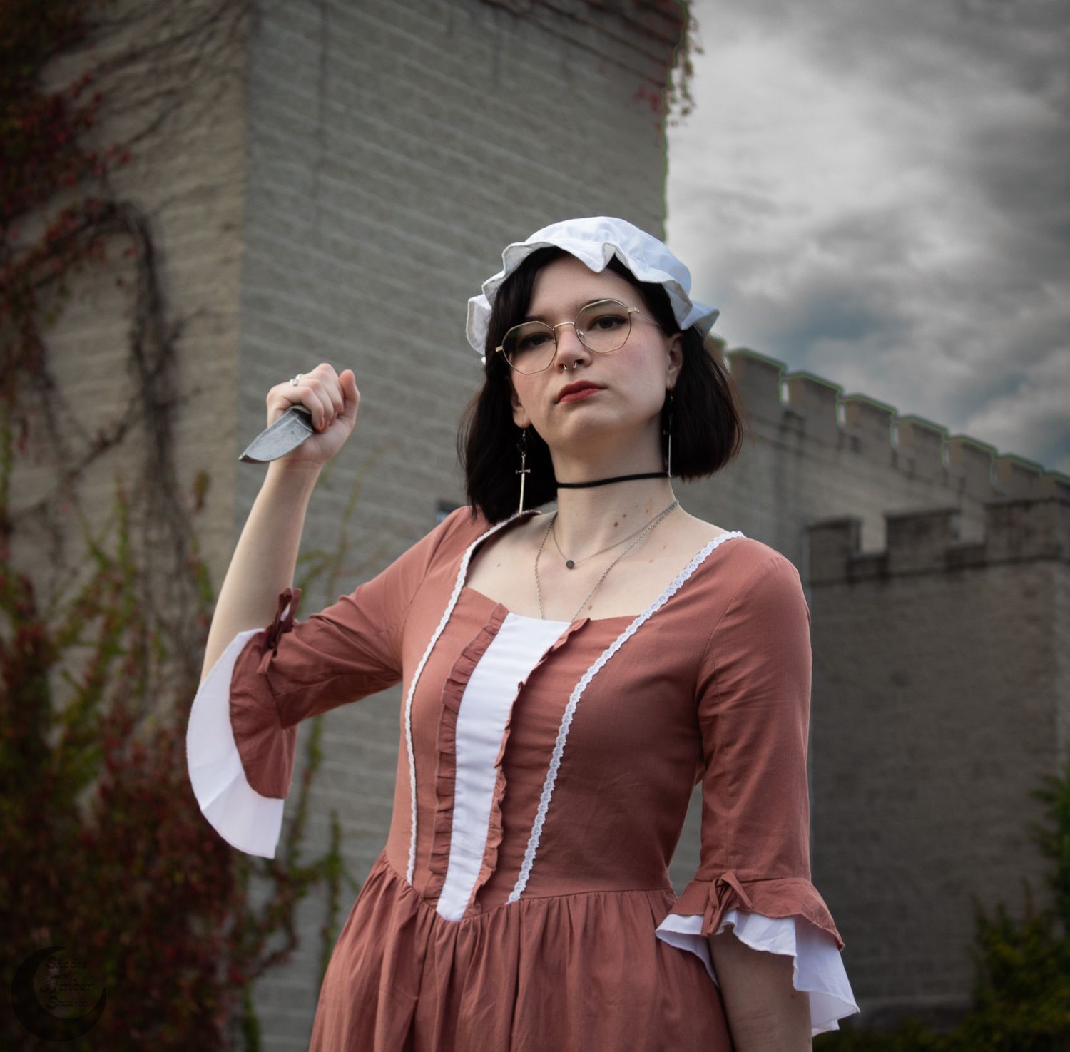 Colonial-era costume featuring dusty rose dress with white trim and cap against castle wall background.