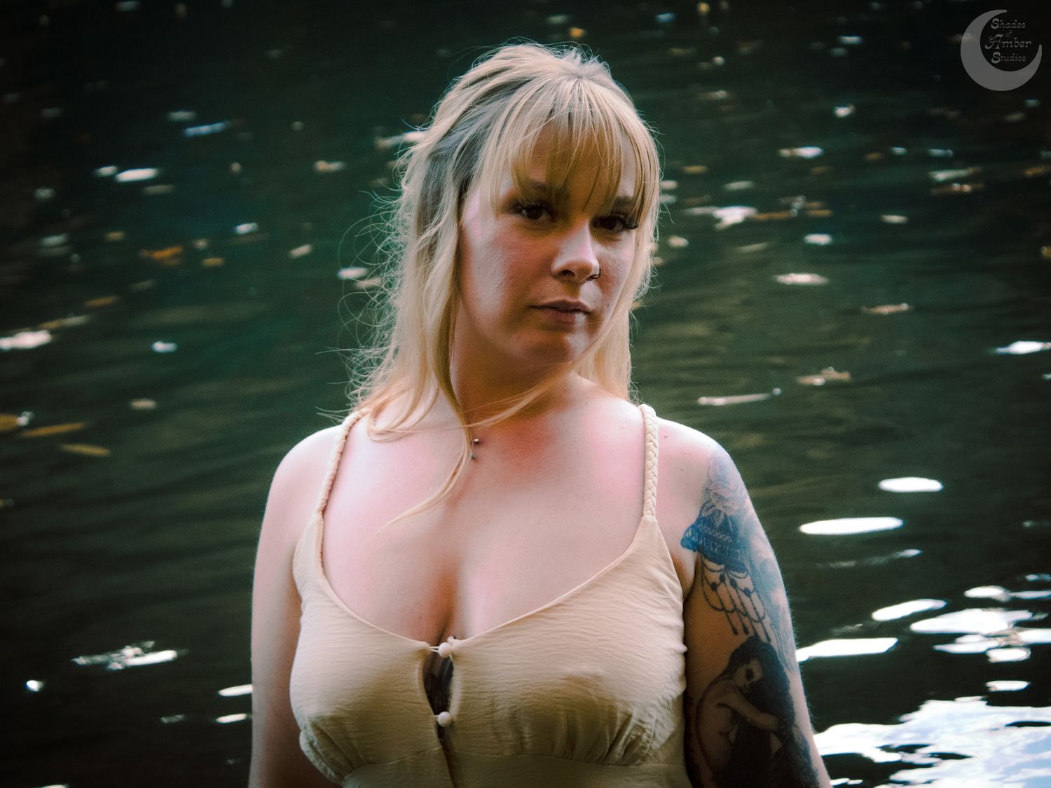 Person in beige corset standing in dark water with tattoos visible.