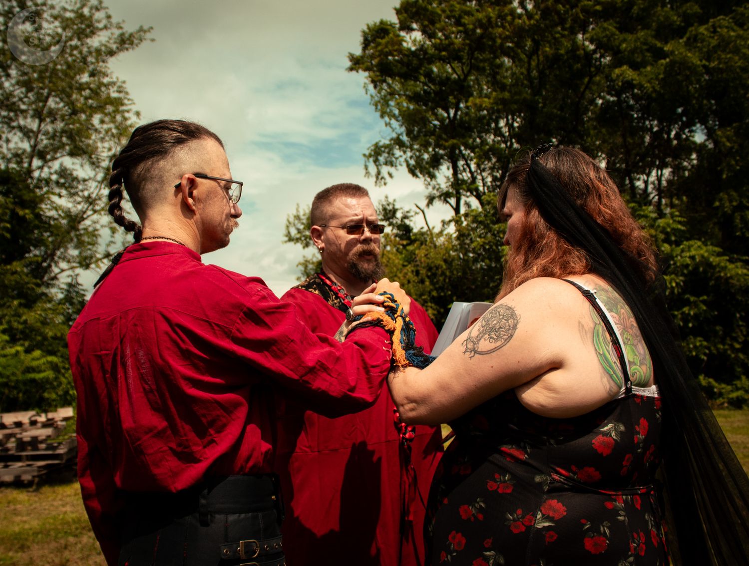 People in red and dark clothing share drinks in a sunny outdoor garden setting.