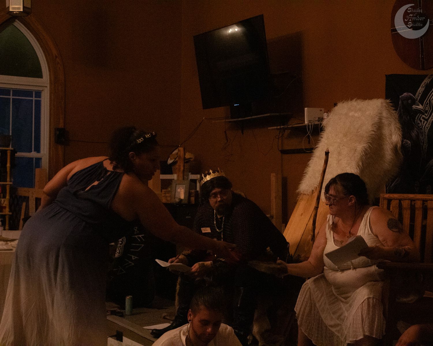 People gathered around a table in a dimly lit room with a TV mounted on the wall in the background.