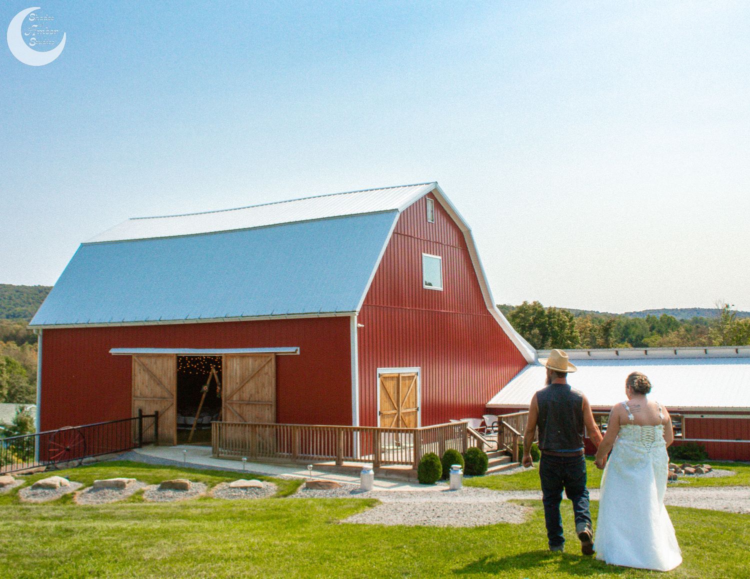 Couple looking at classic red barn on hillside during country wedding photoshoot.