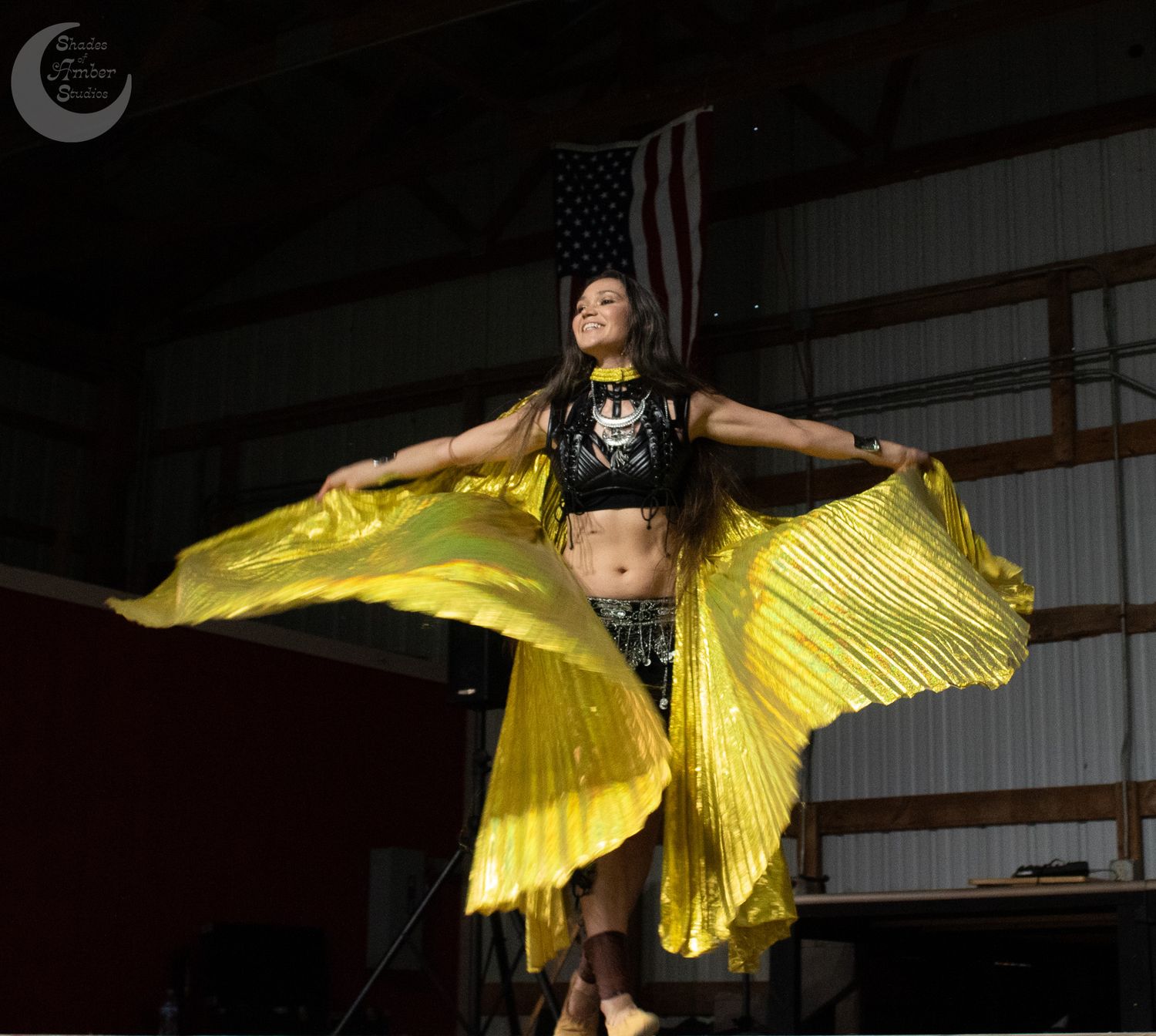 Ballet dancer performs graceful moves wearing vibrant yellow wings in atmospheric dark performance space.