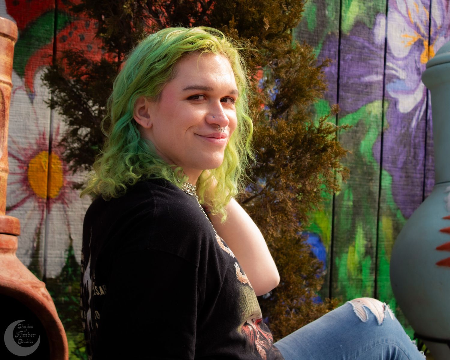 Casual portrait with vibrant green hair against floral mural background.