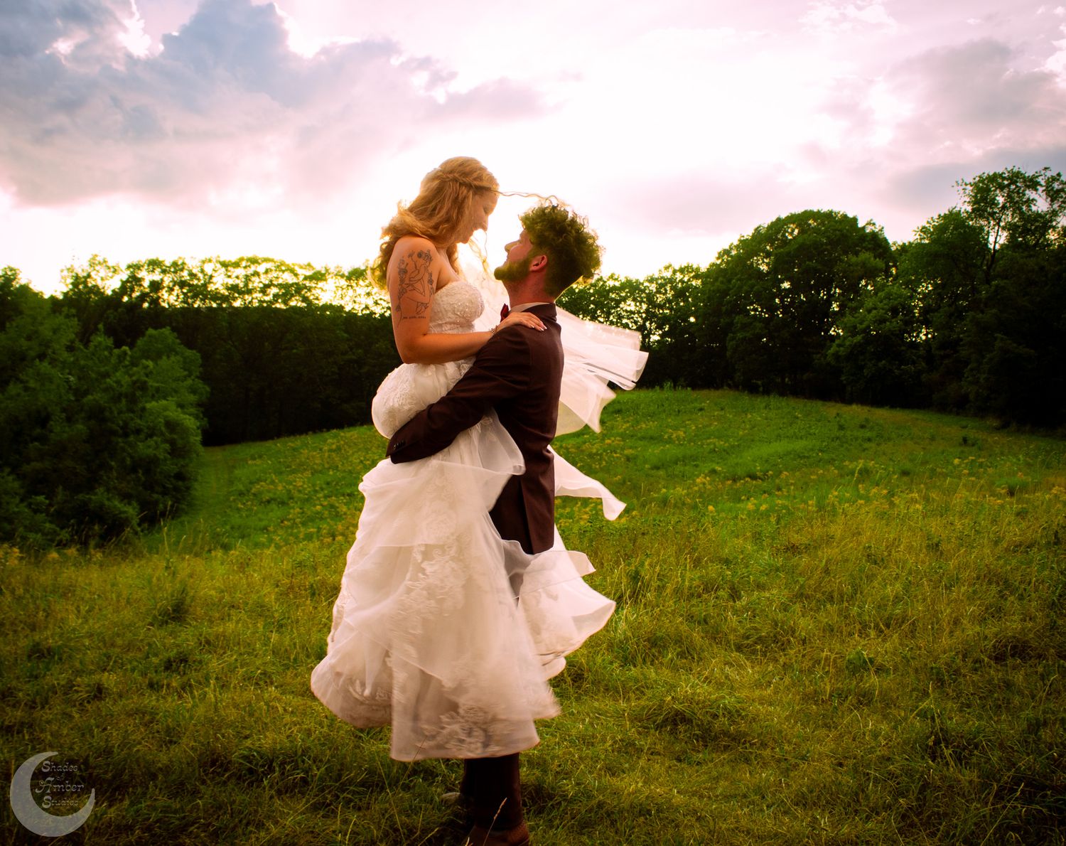 Wedding couple embracing in a rural field at sunset with dramatic sky.