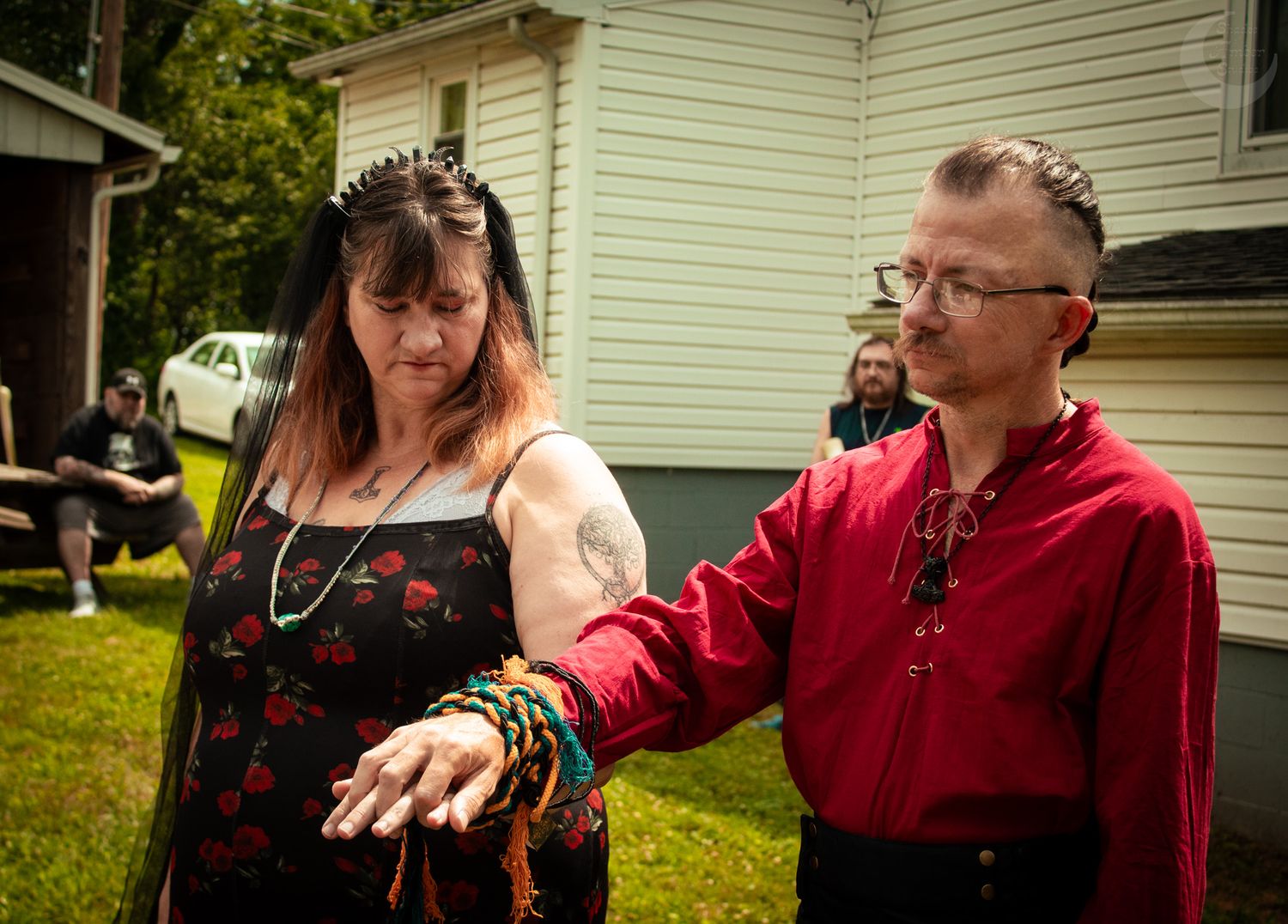 Two people examine a small snake outdoors in front of a white house on a grassy lawn.